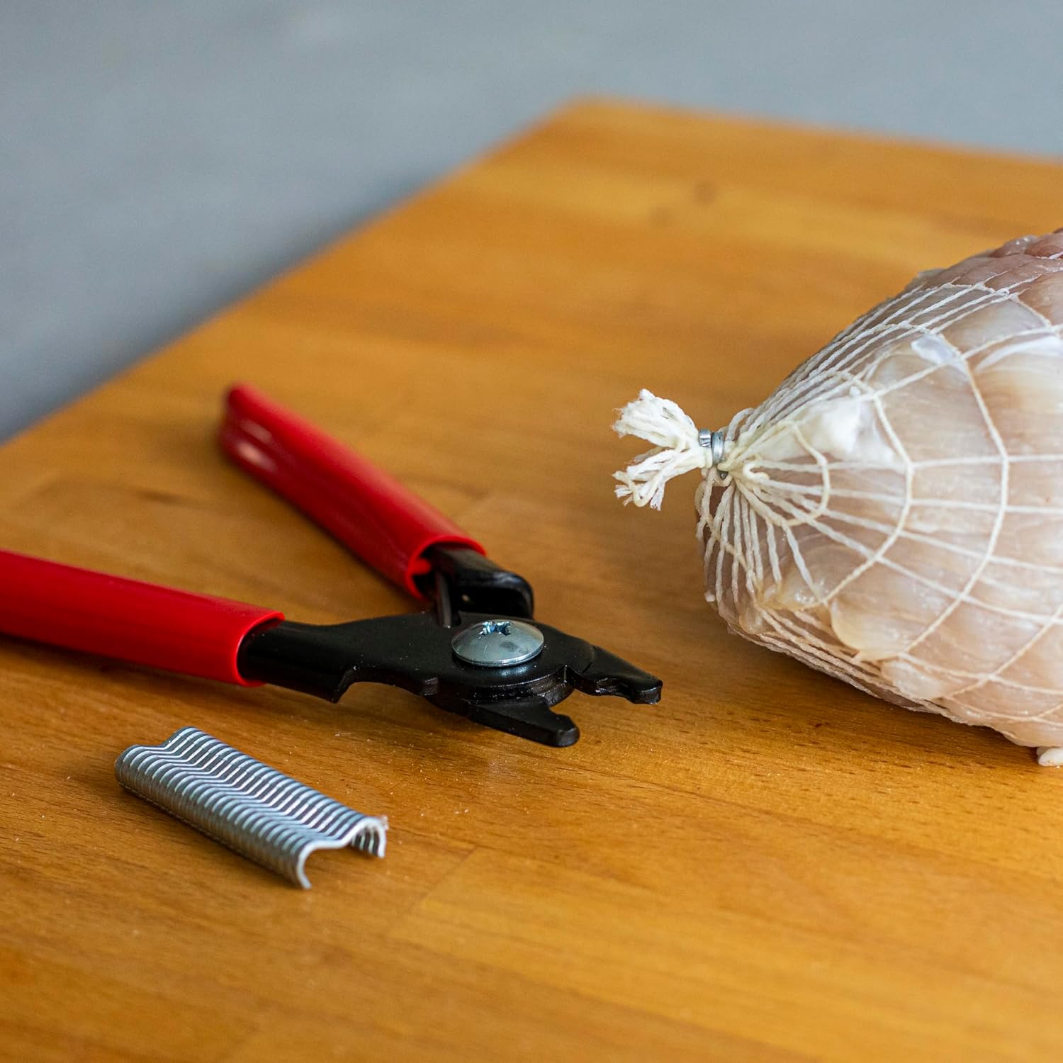 A securely clipped netted meat product on a wooden surface, with the Browin 313313 Sausage Clipper and remaining clips nearby.