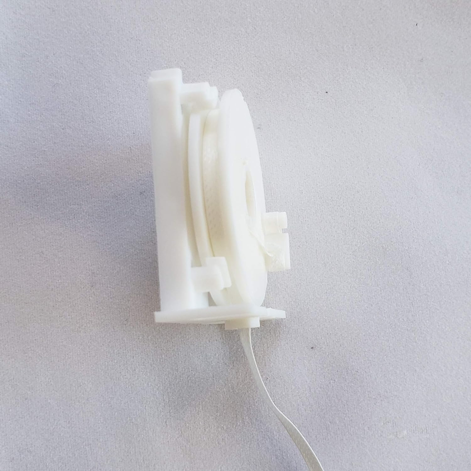 ด้านข้าง view of a white spool with flat tape from the HunterDouglas Restring Kit.