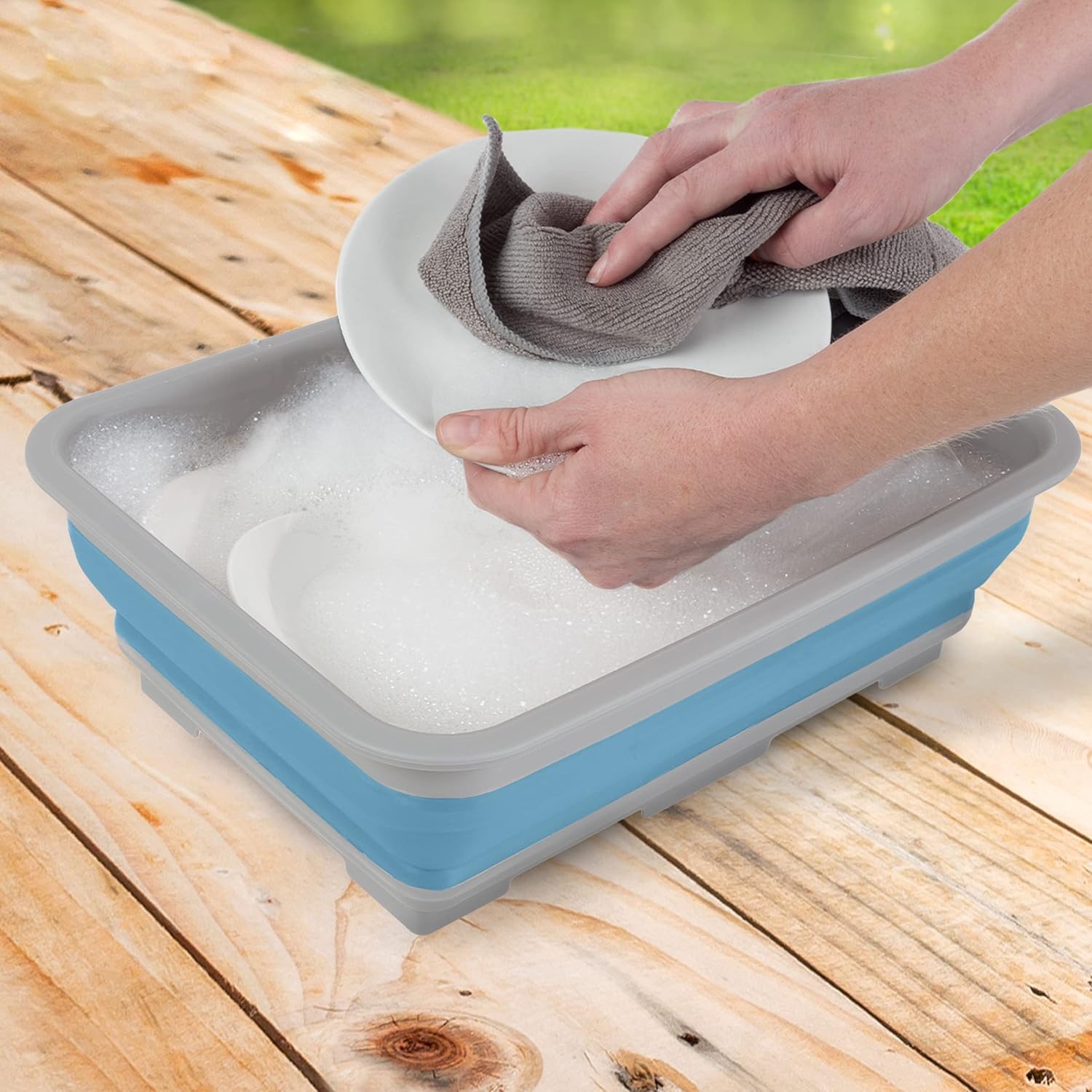 Hands washing a plate in the expanded blue and gray collapsible camp sink.