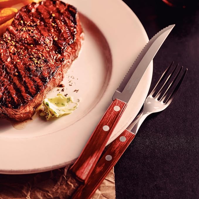Faca e garfo Tramontina Polywood apoiados em um prato branco ao lado de um bife de carne grelhada com manteiga de ervas.