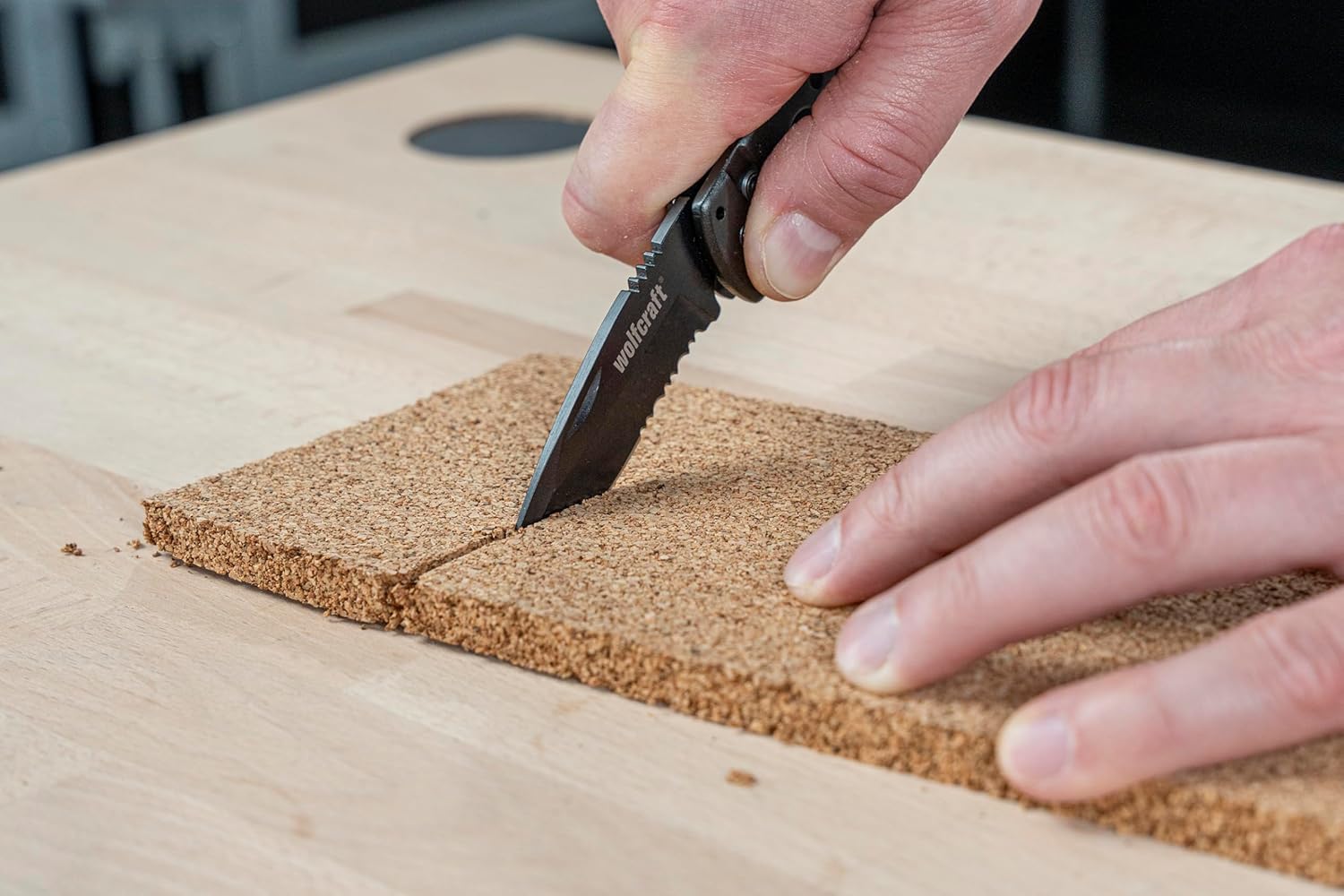The wolfcraft 4289000 Folding Pocket Knife's smooth blade cutting through a piece of cork.