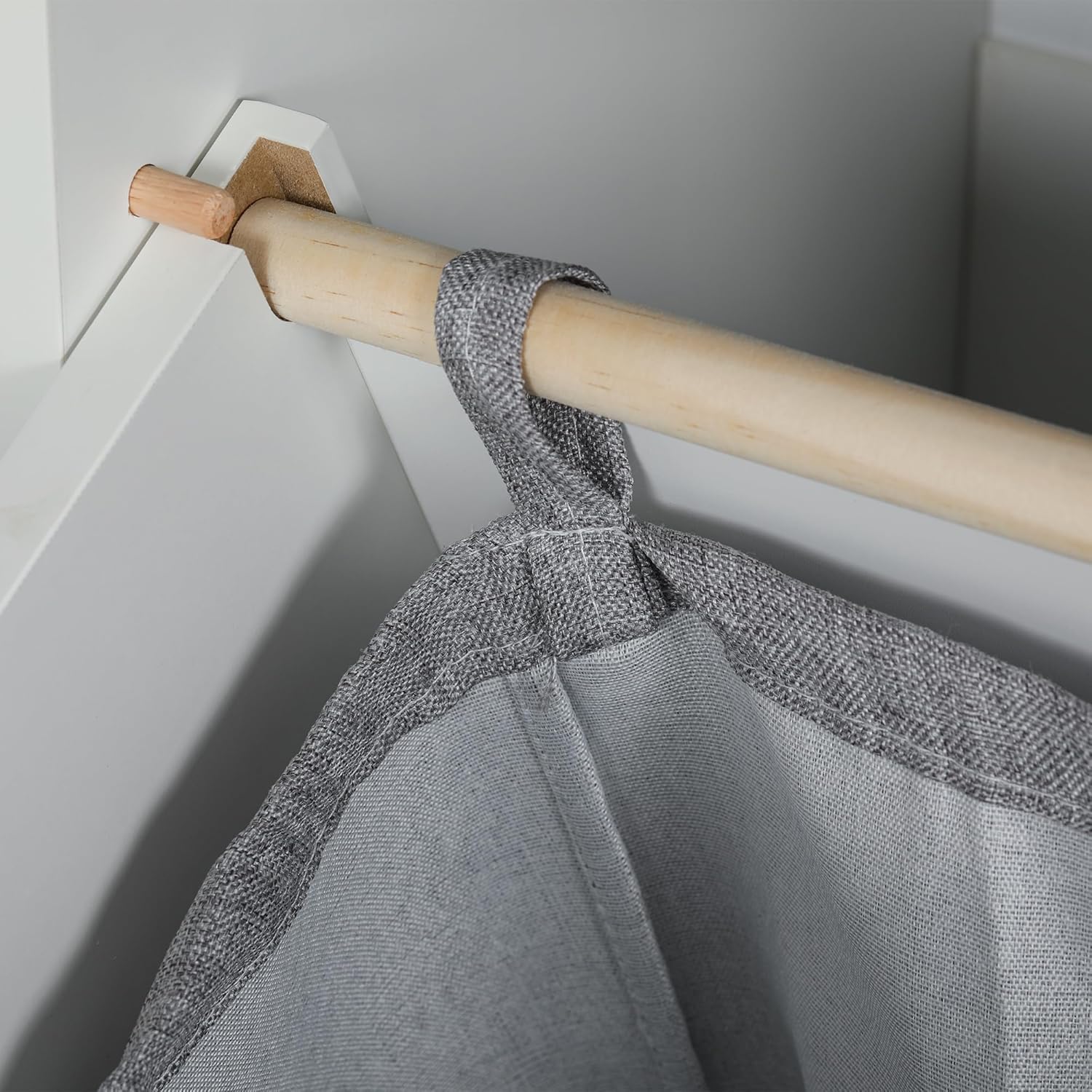 Close-up of the fabric laundry basket attached to the wooden rod inside the cabinet.
