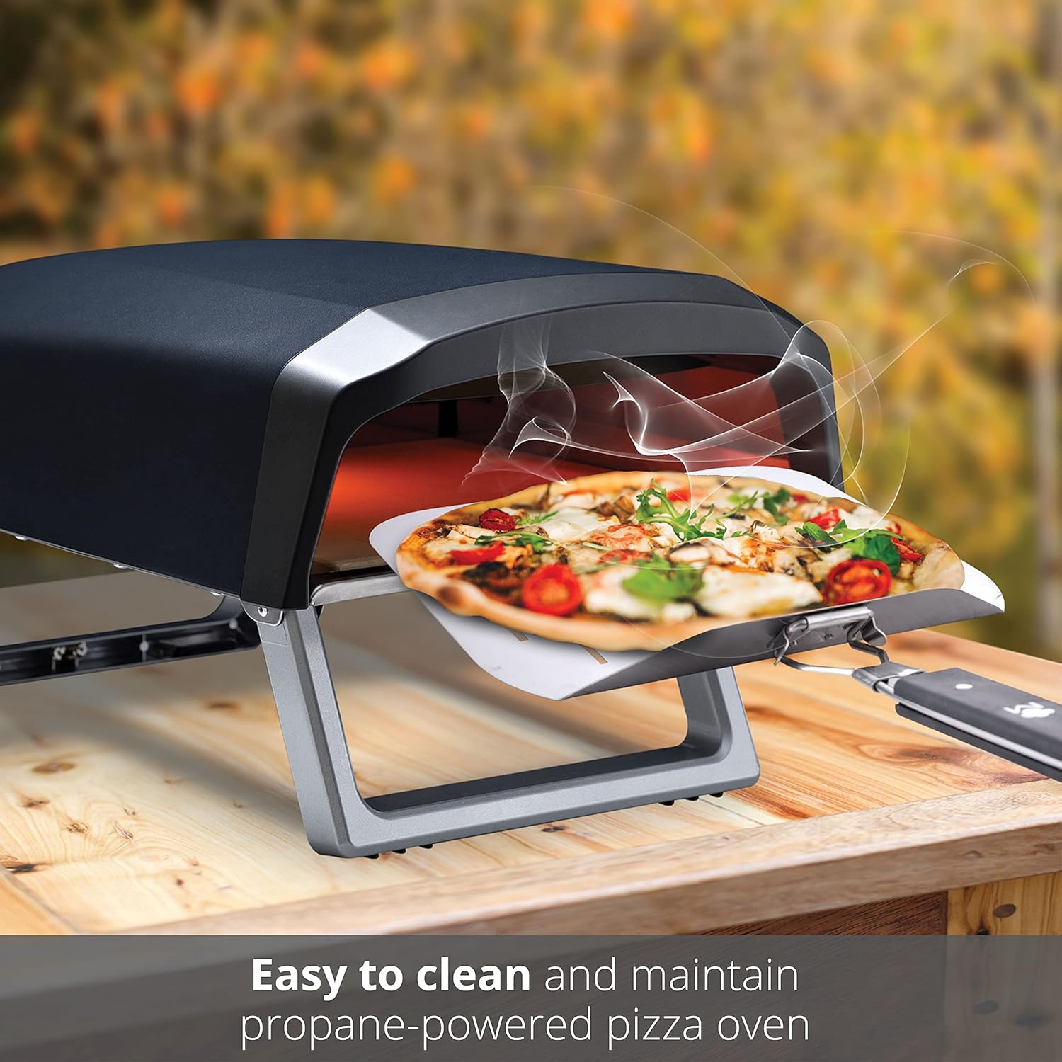 A pizza being slid into the MasterPRO Outdoor Pizza Oven using a pizza peel, with steam rising from the oven.