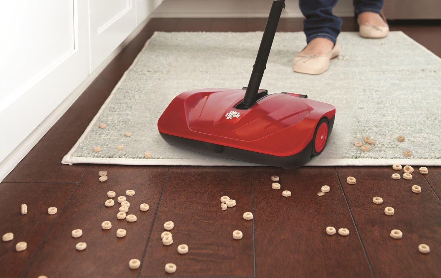 Dirt Devil Simpli-Sweep Manual Push Sweeper cleaning cereal on a hard floor.