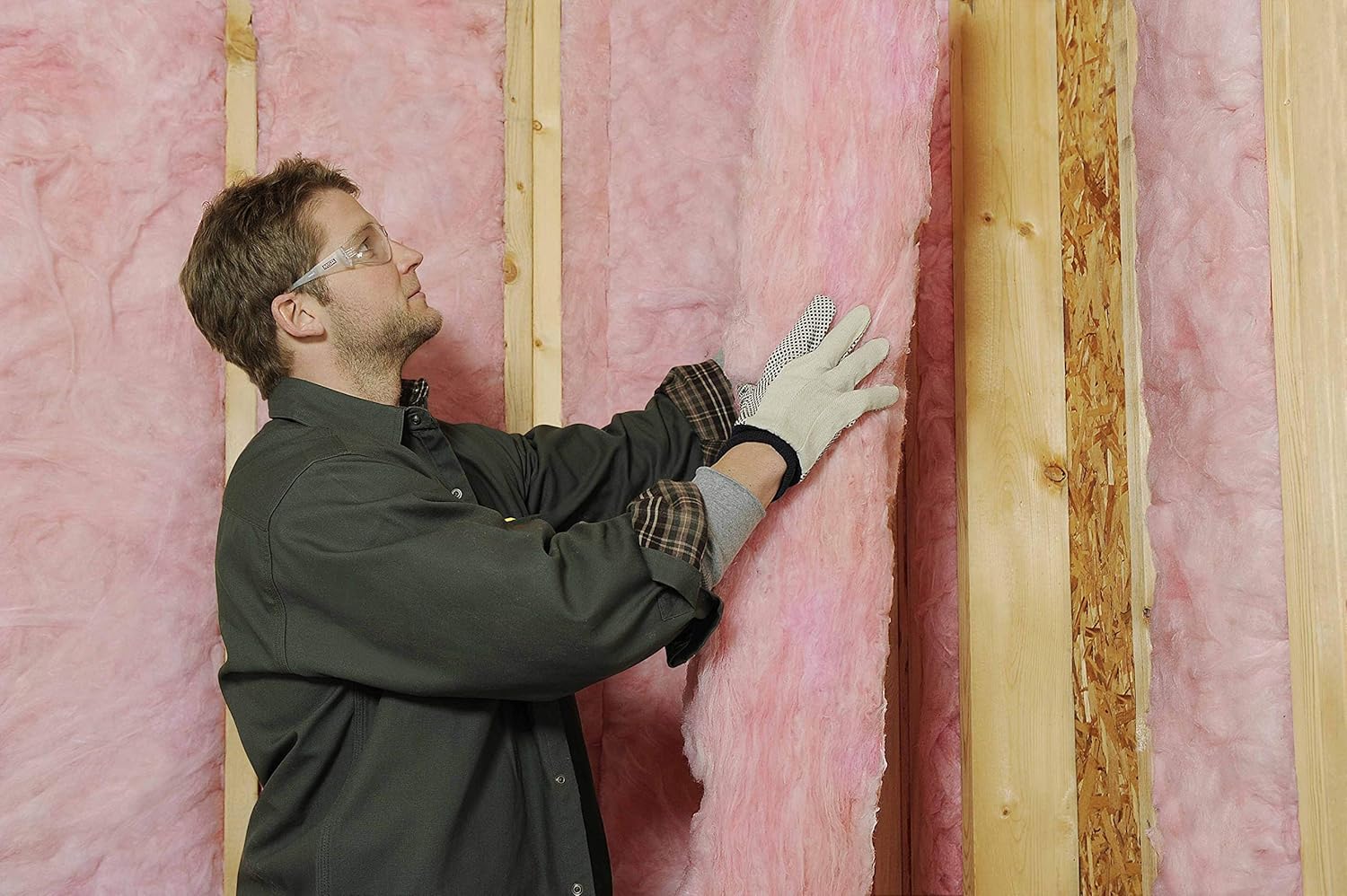 Man installing Owens Corning fiberglass insulation into a wall cavity