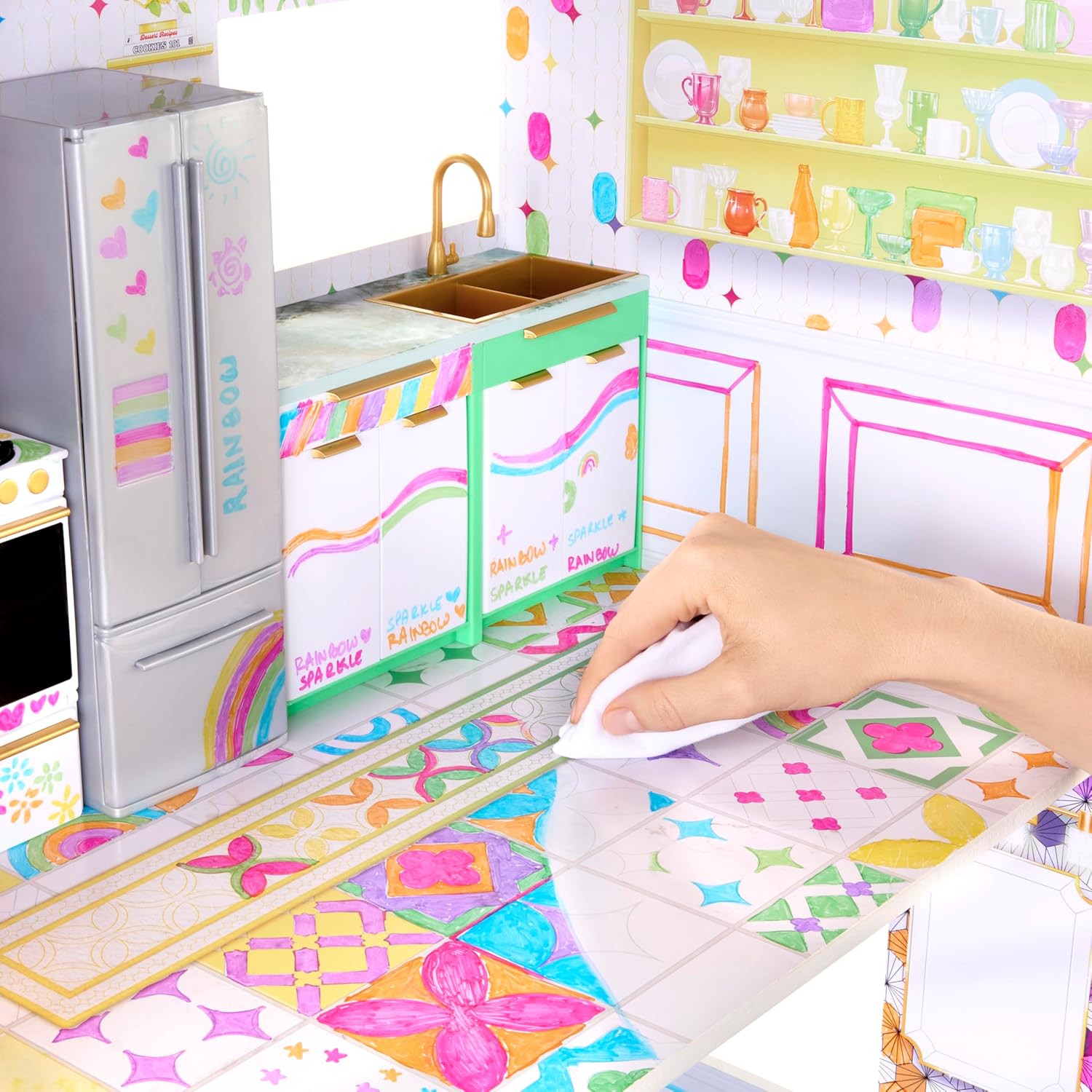 A hand erasing a design from the kitchen floor of the dollhouse with a white cloth.