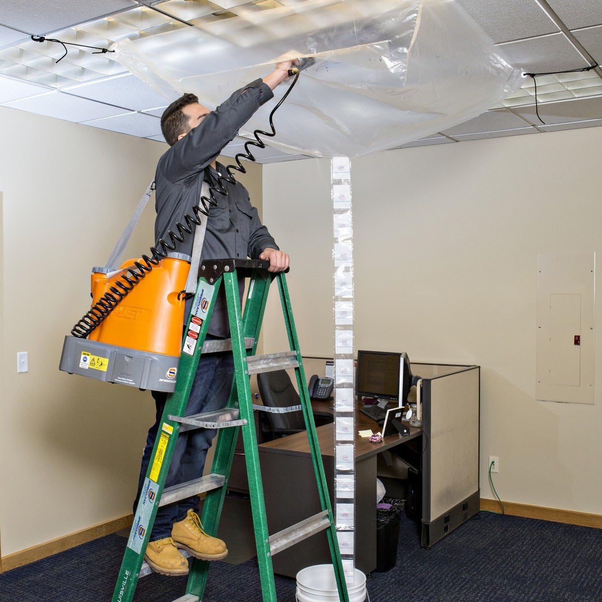 Technician cleaning a ceiling-mounted HVAC unit with the SpeedClean CoilJet, using a ladder and coil bib.