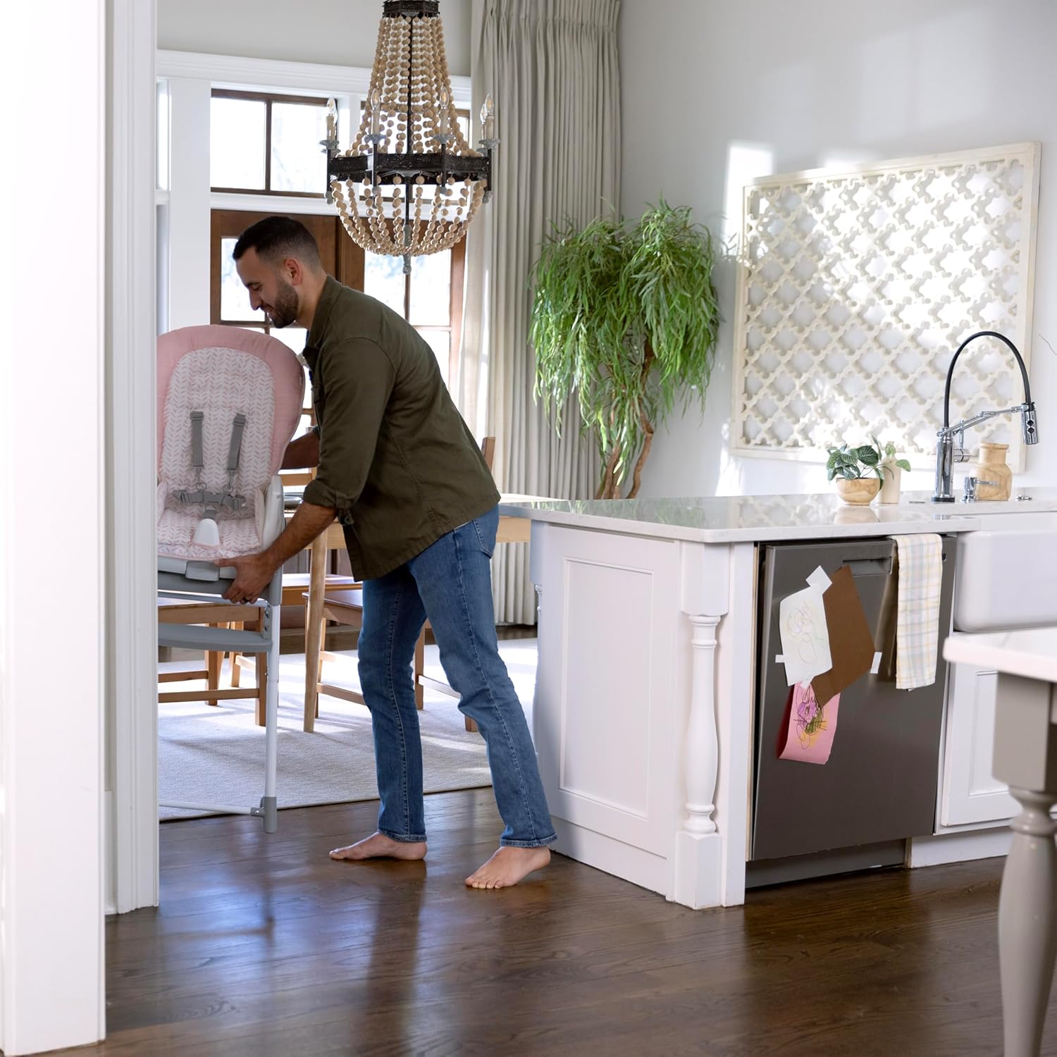 A person demonstrating the foldaway feature of the high chair in a kitchen setting.
