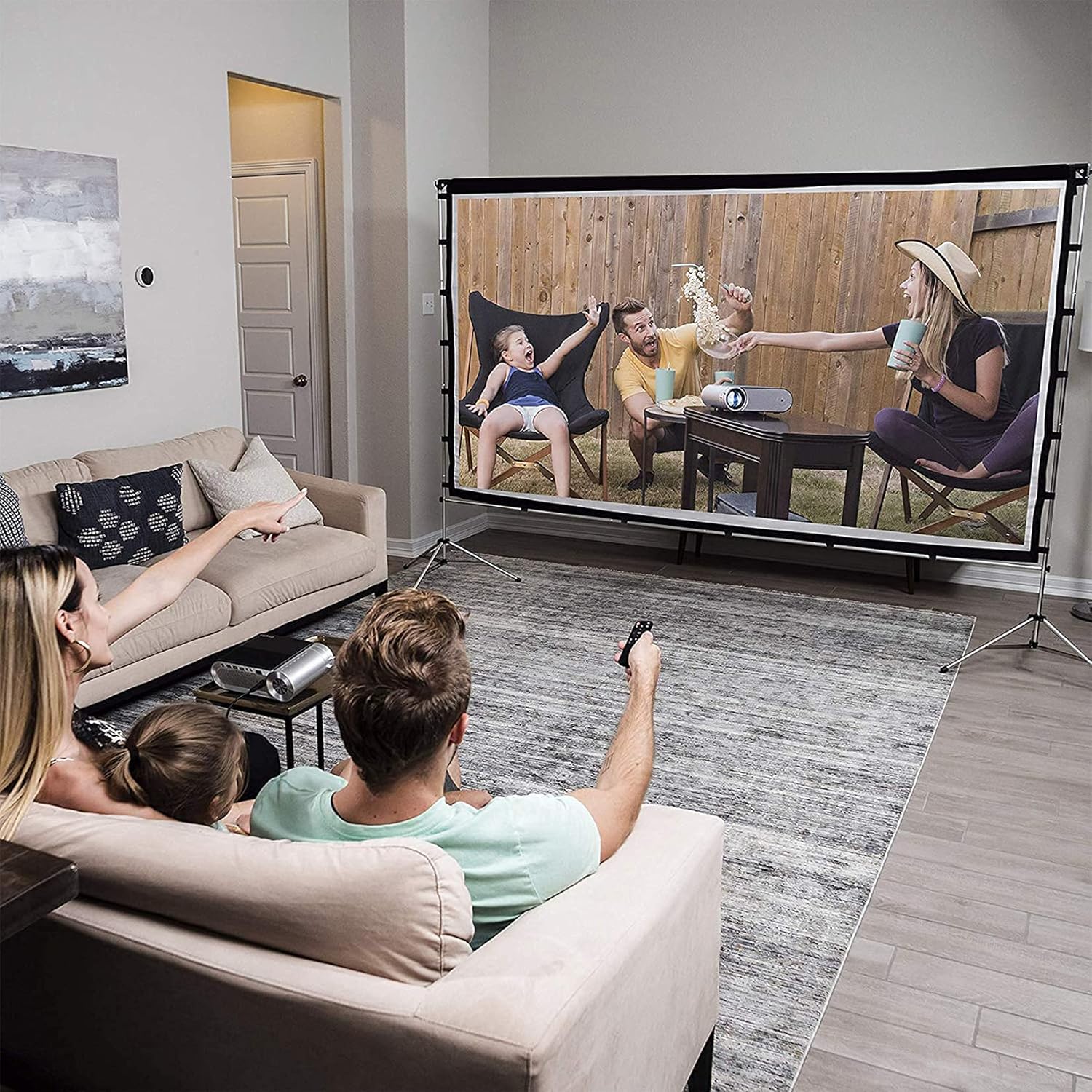 Family watching a movie on the Vamvo 100-inch projector screen in a living room setting.