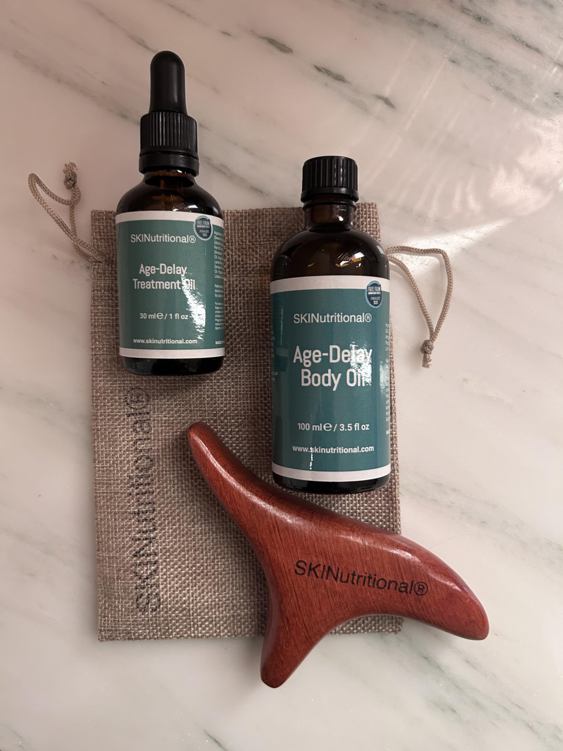 Age-Delay Body Oil (100ml) and Face and Neck Treatmenet Oil (30ml) Set by SKINutritional. Comes with wooden Gua Sha lymphatic massage tool for face and body together with oils in a jute pouch