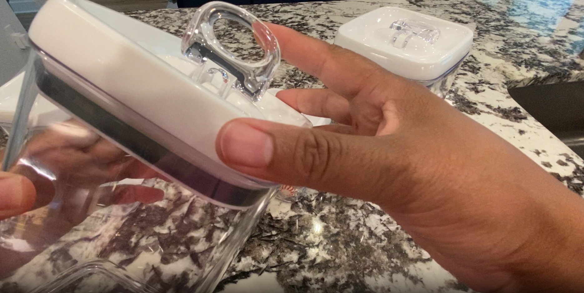 A hand demonstrating how to open the flip-top lid of a Better Homes & Gardens container filled with coffee grounds.