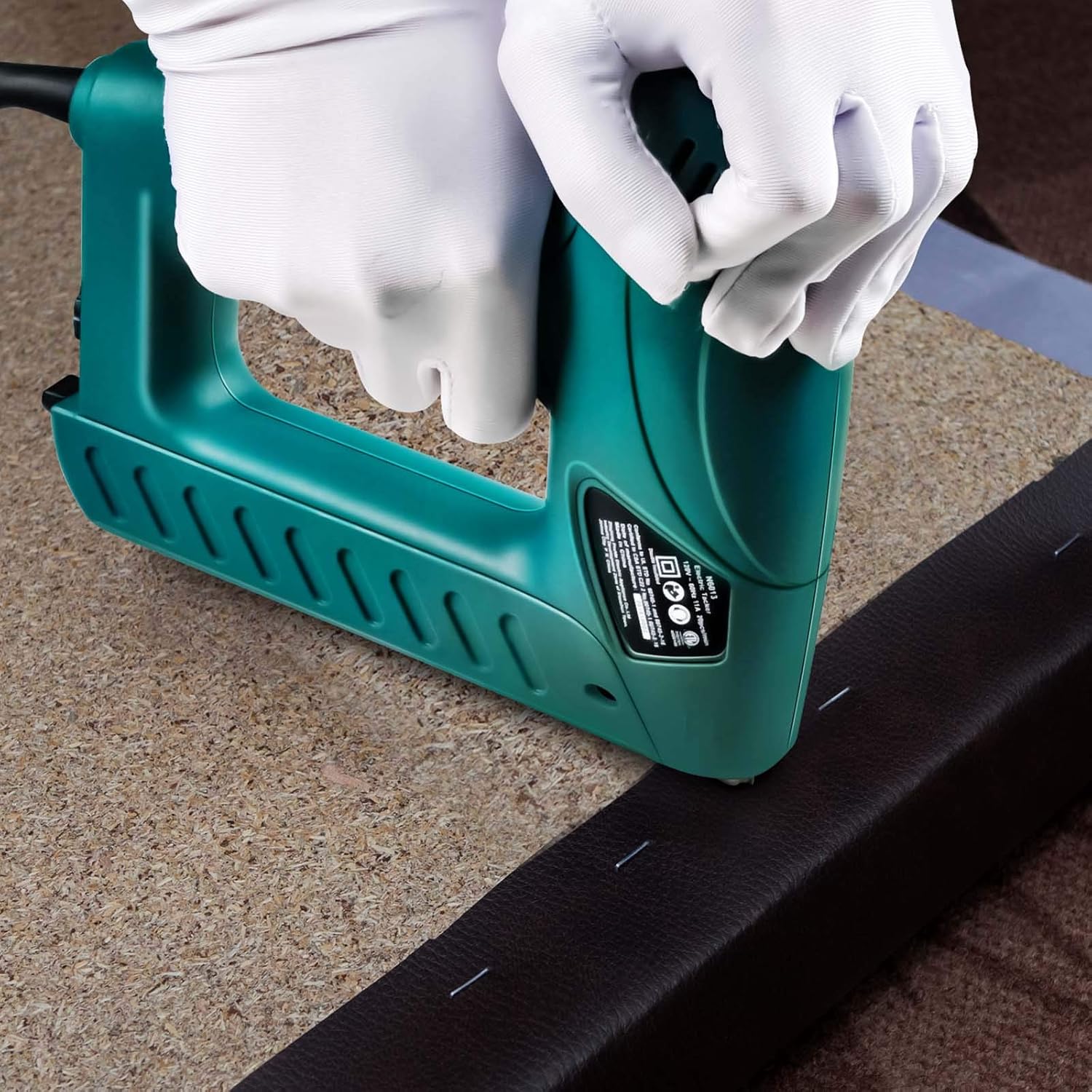 A person using a NEU MASTER electric staple gun to fasten material onto a cork board, demonstrating application.