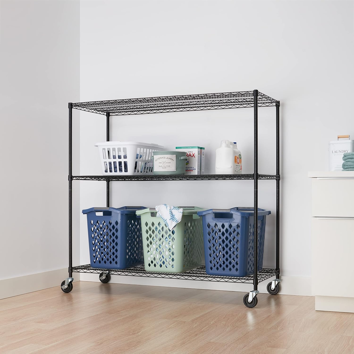 TRINITY Basics 3-Tier Wire Shelving Unit with Wheels, fully assembled and loaded with laundry baskets and supplies.