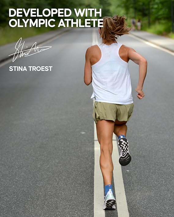 A rear view of Olympic athlete Stina Troest running on a road, wearing one pair of the Danish Endurance Cushioned Running Socks, a white sleeveless top, and green shorts. The image includes text that reads 