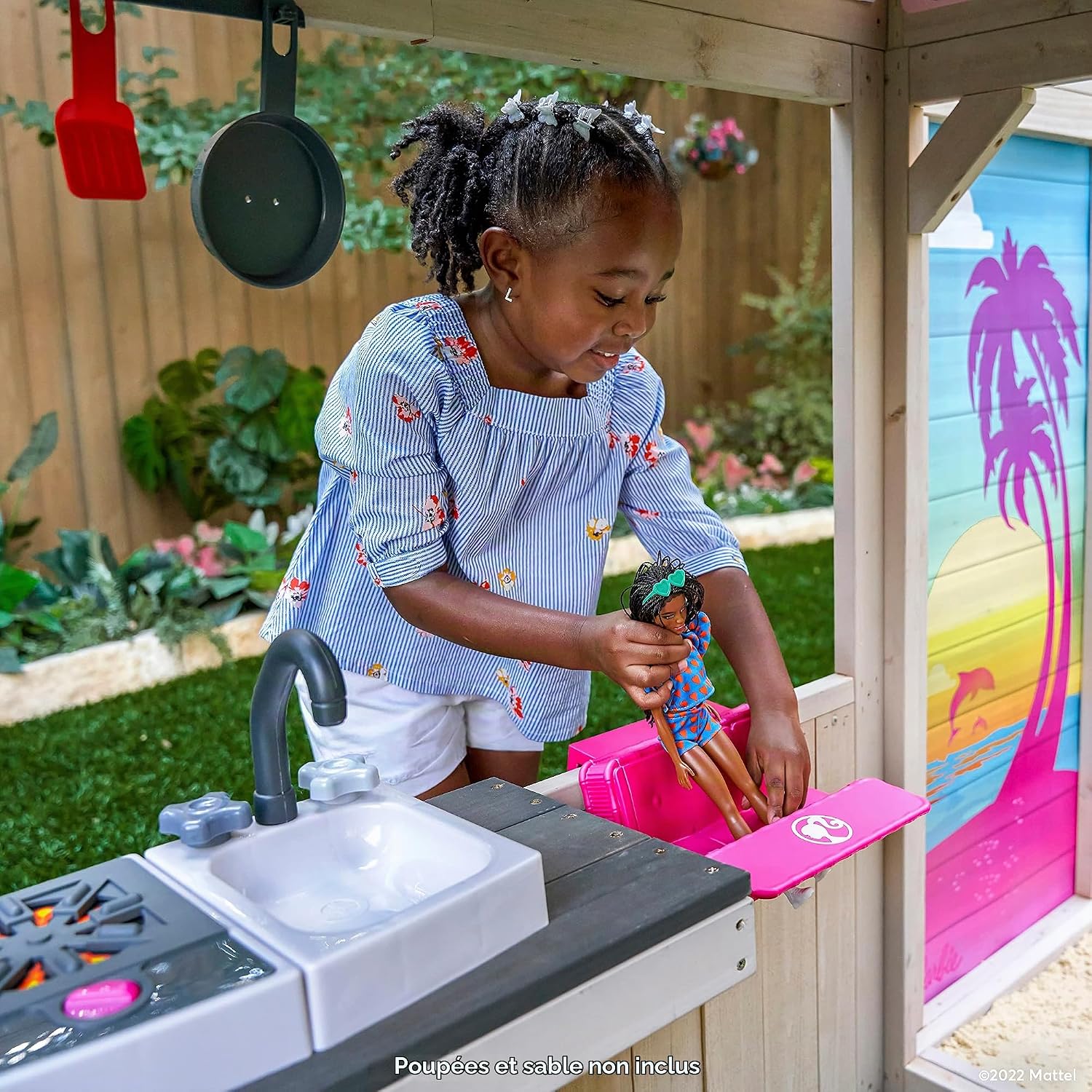 A child placing a Barbie doll on a pink doll-sized picnic table attached to the playhouse counter.