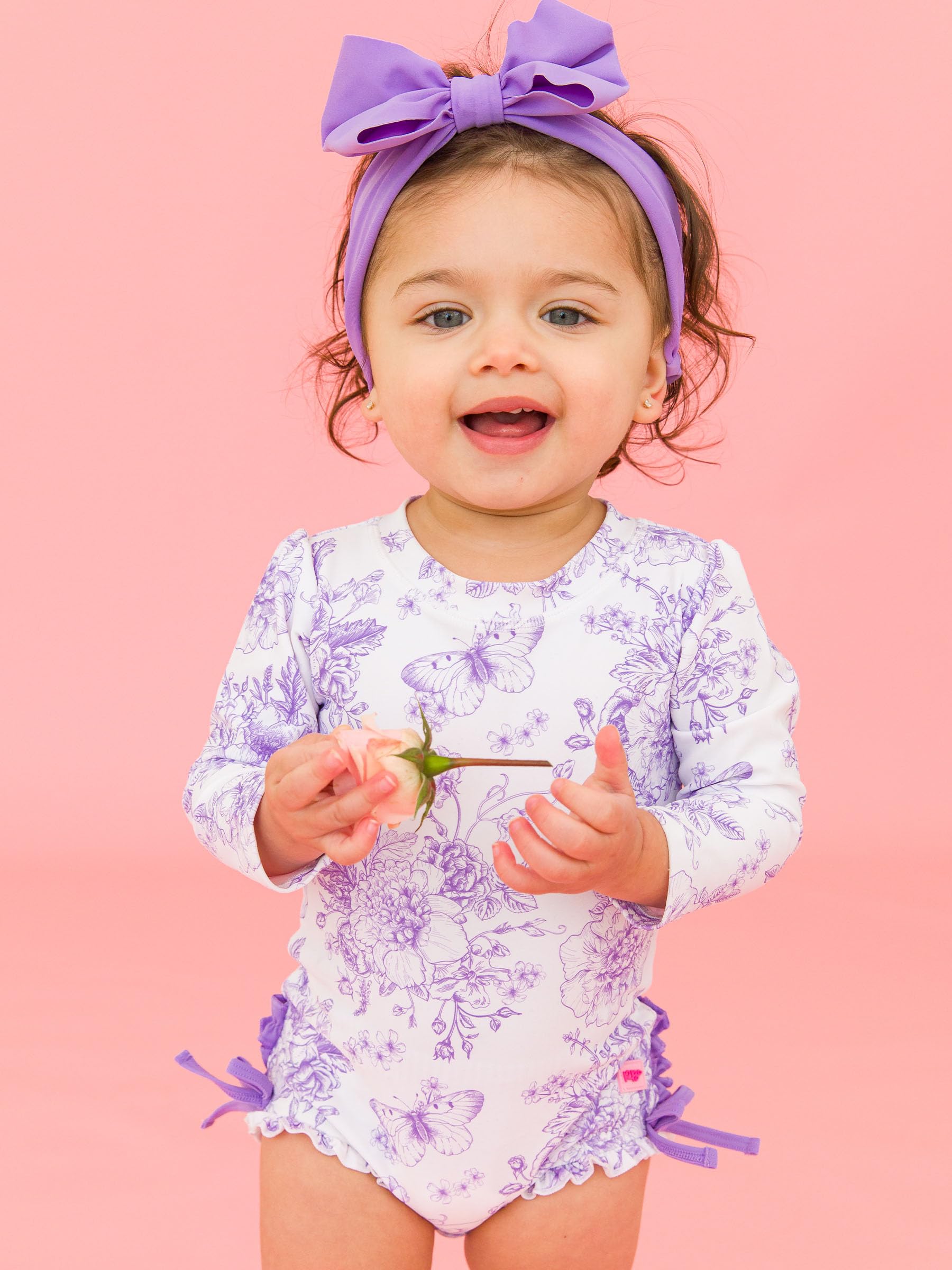 RuffleButts Costume da Bagno Intero A Maniche Lunghe con Stampa Floreale E Protezione Solare UPF 50 per Bambine, con Cerniera, Motivo Giardino di Farfalle Viola Glicine, 18-24 Mesi