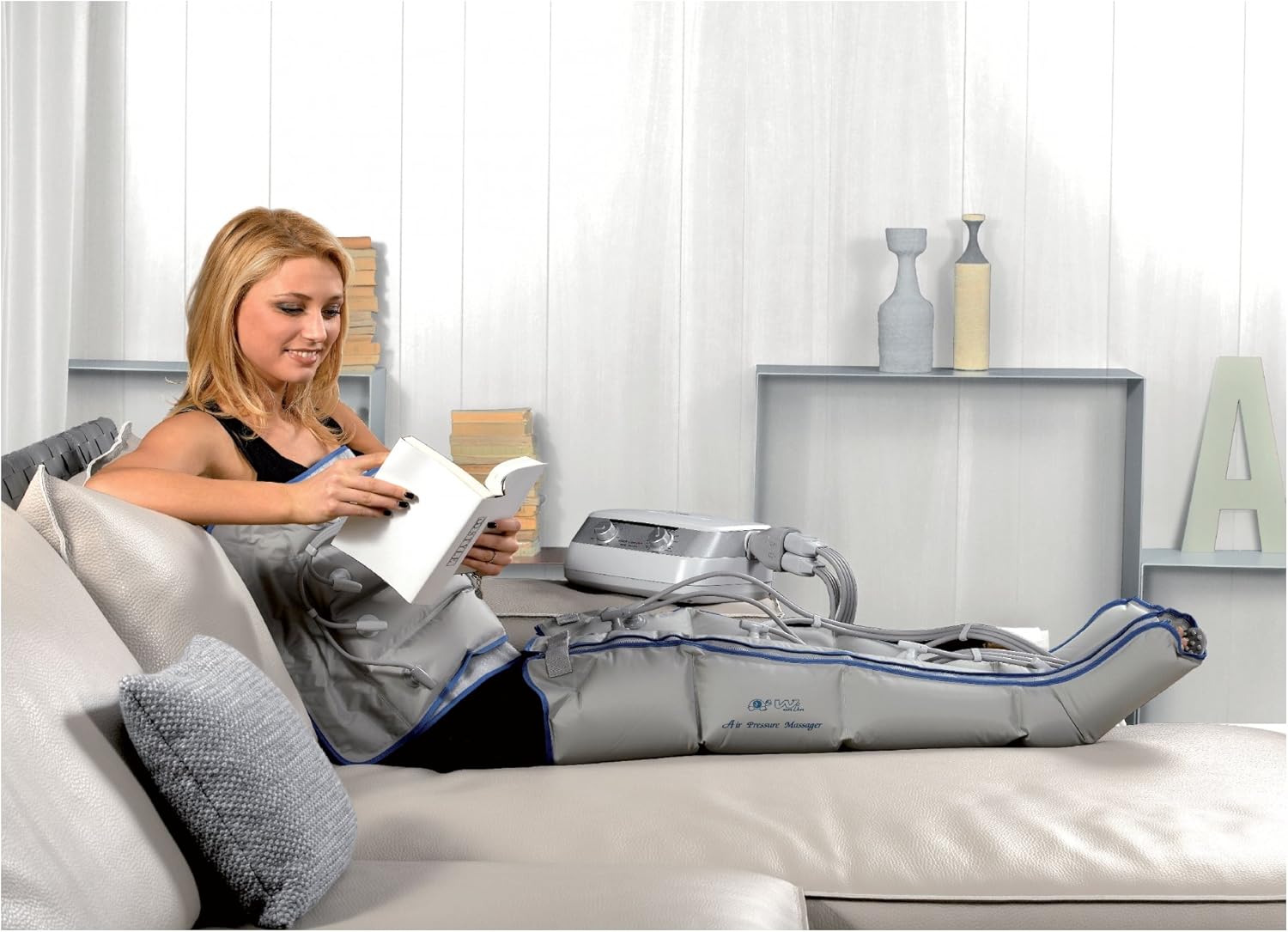 A woman reading a book while undergoing pressotherapy treatment with leg sleeves.