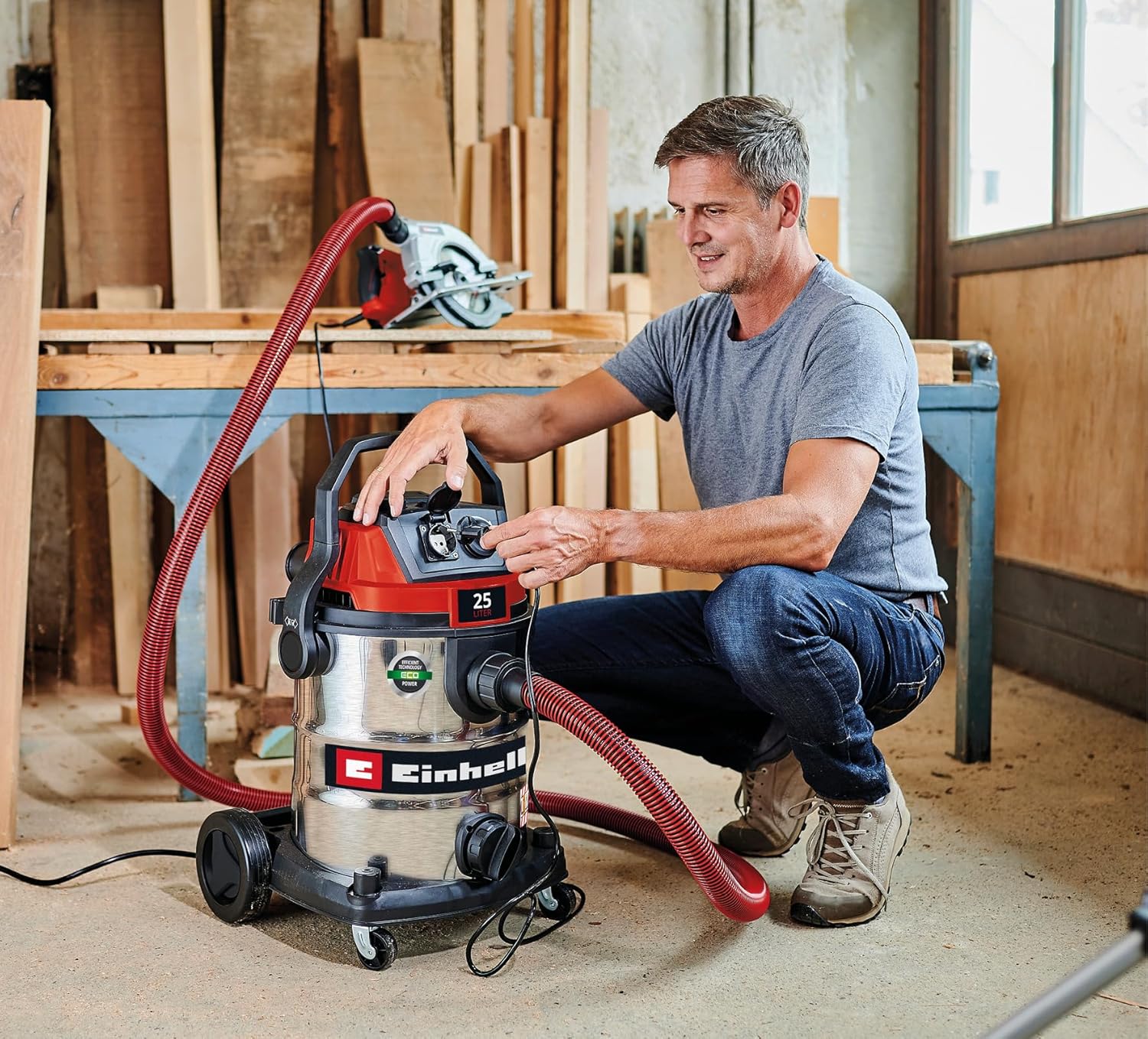 Man operating the Einhell TE-VC 2580 SACL wet and dry vacuum cleaner in a workshop setting.