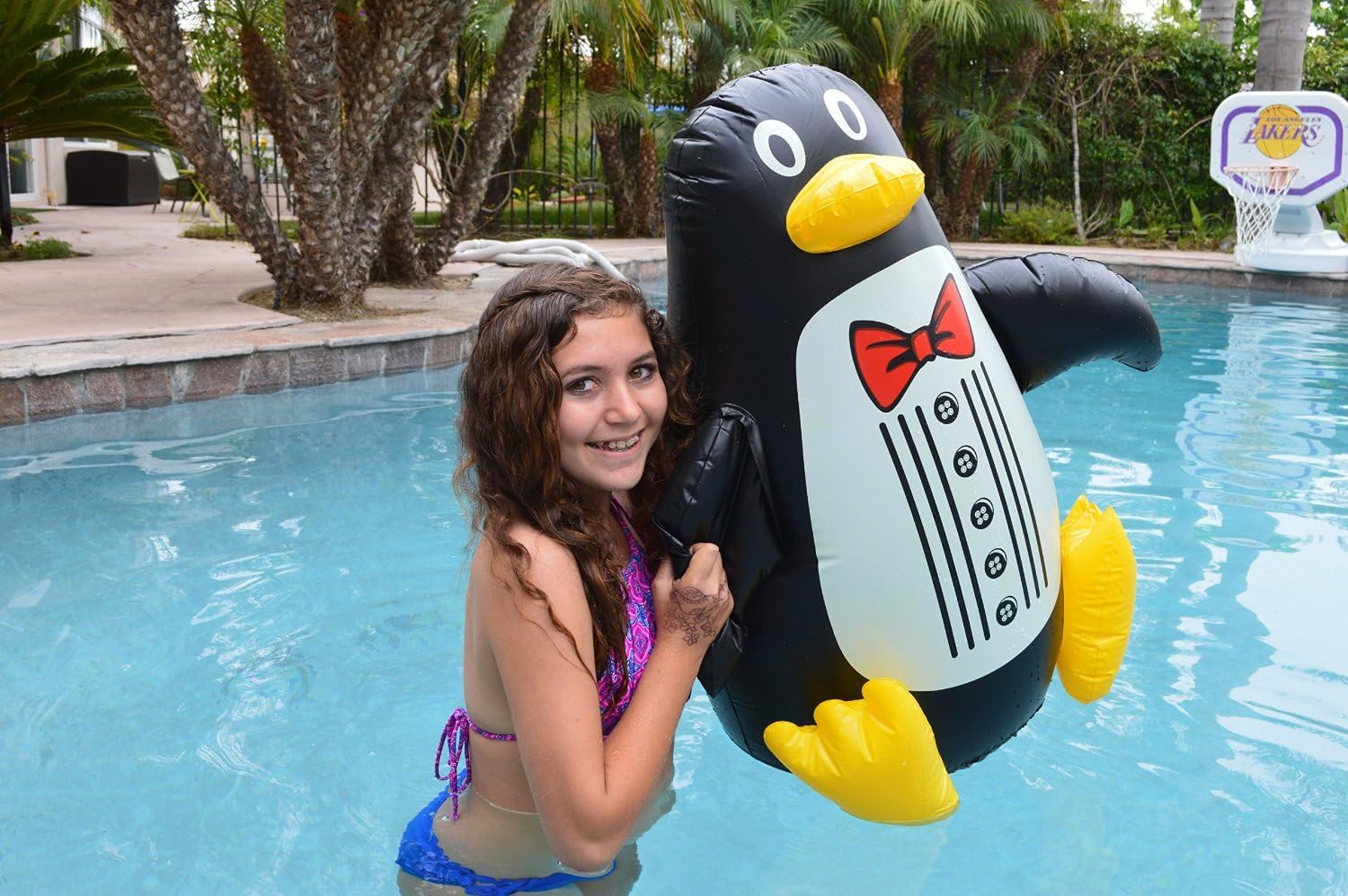 Girl smiling next to the Poolmaster Floating Penguin in a swimming pool