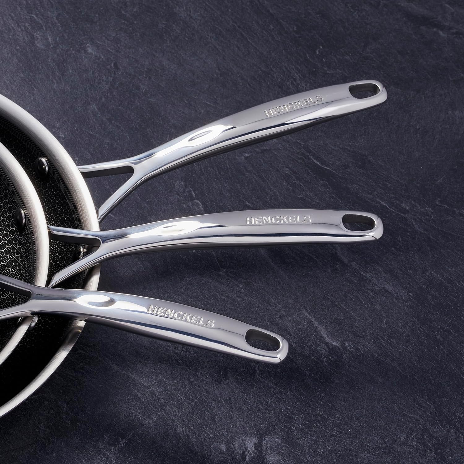Close-up of the ergonomic, stay-cool stainless steel handle of a Henckels Paradigm fry pan, showing the HENCKELS logo.