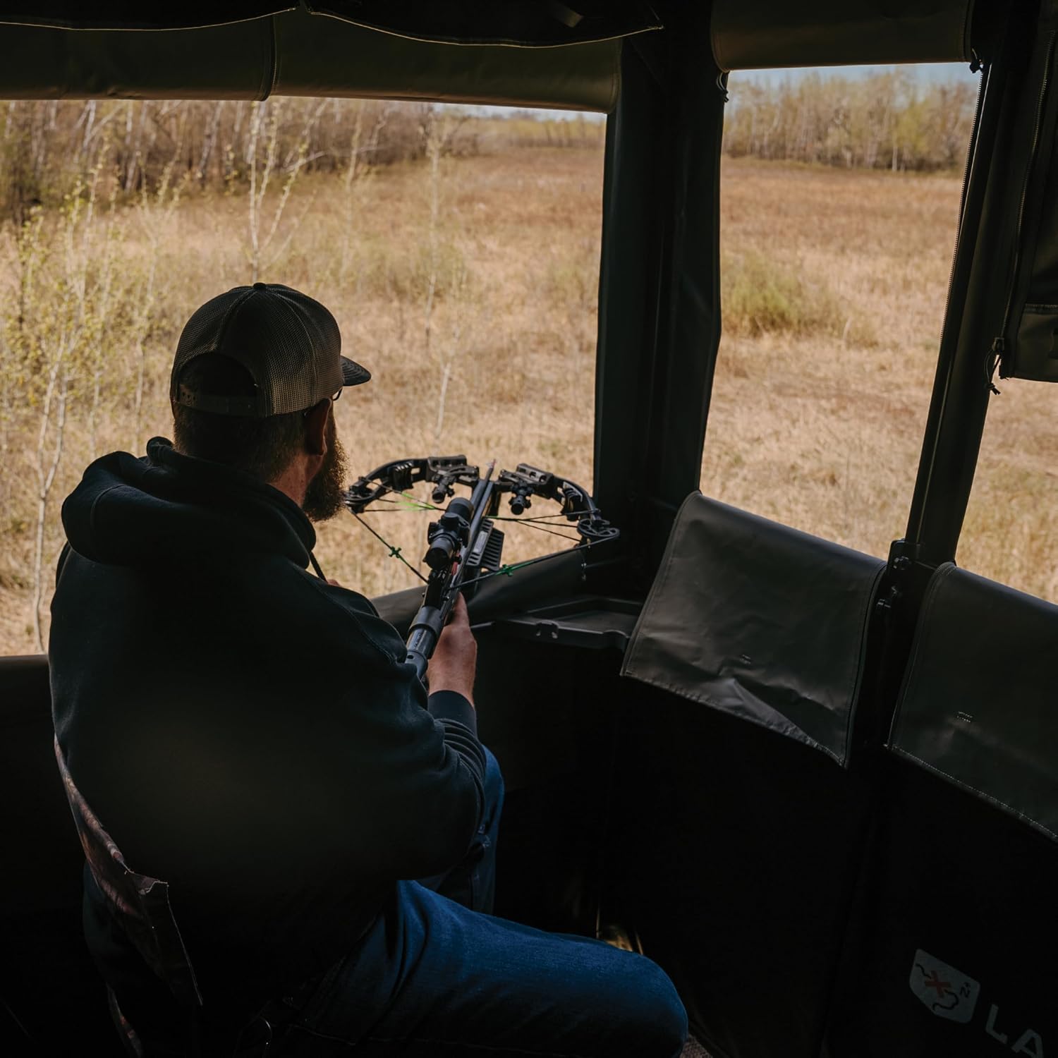 Hunter inside the blind with a crossbow, looking out a window