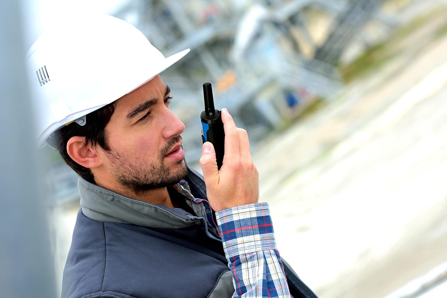 A person in a hard hat holding an Alecto FR-175BW radio to their ear, listening.