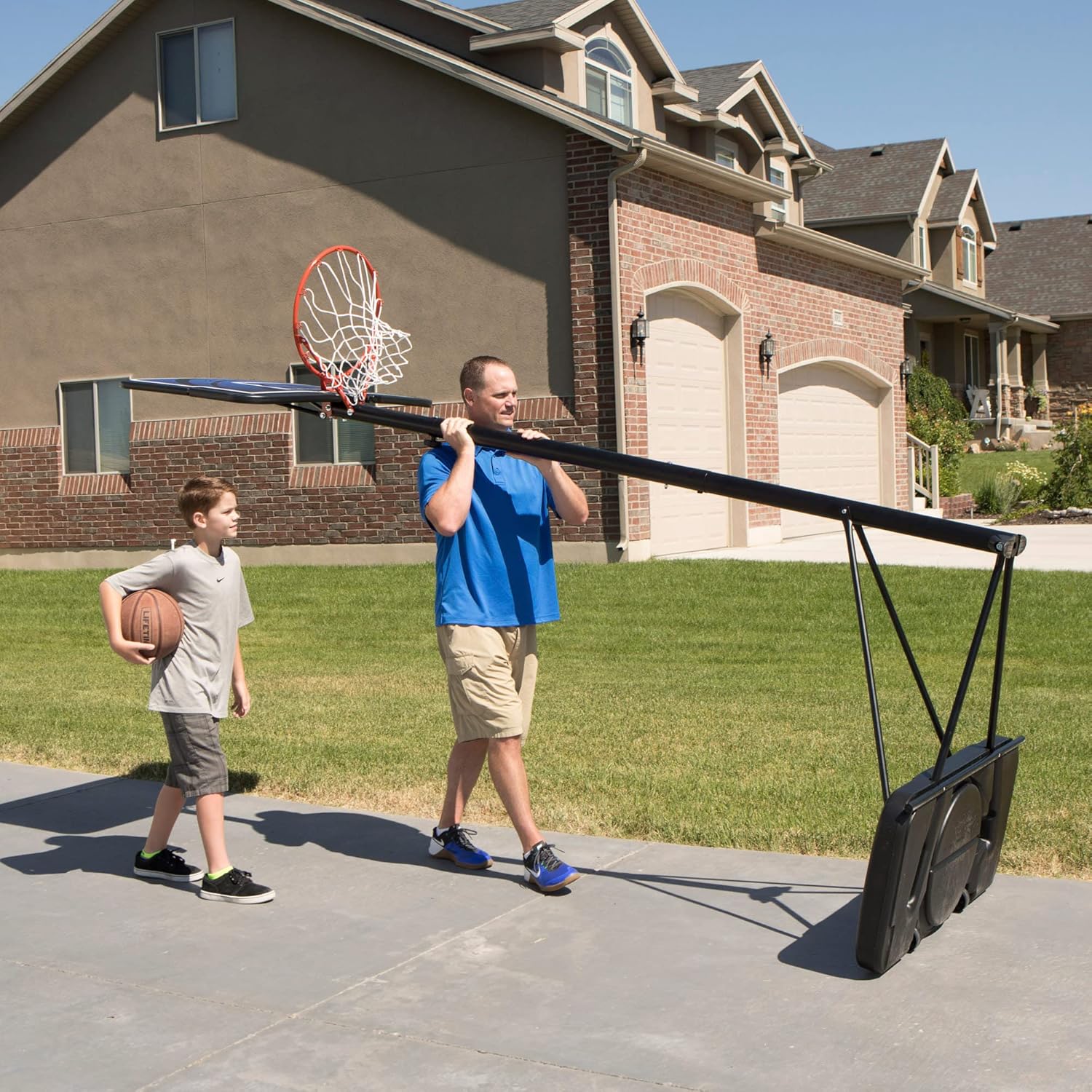 A person tilting the basketball system to move it using the integrated wheels on the base.
