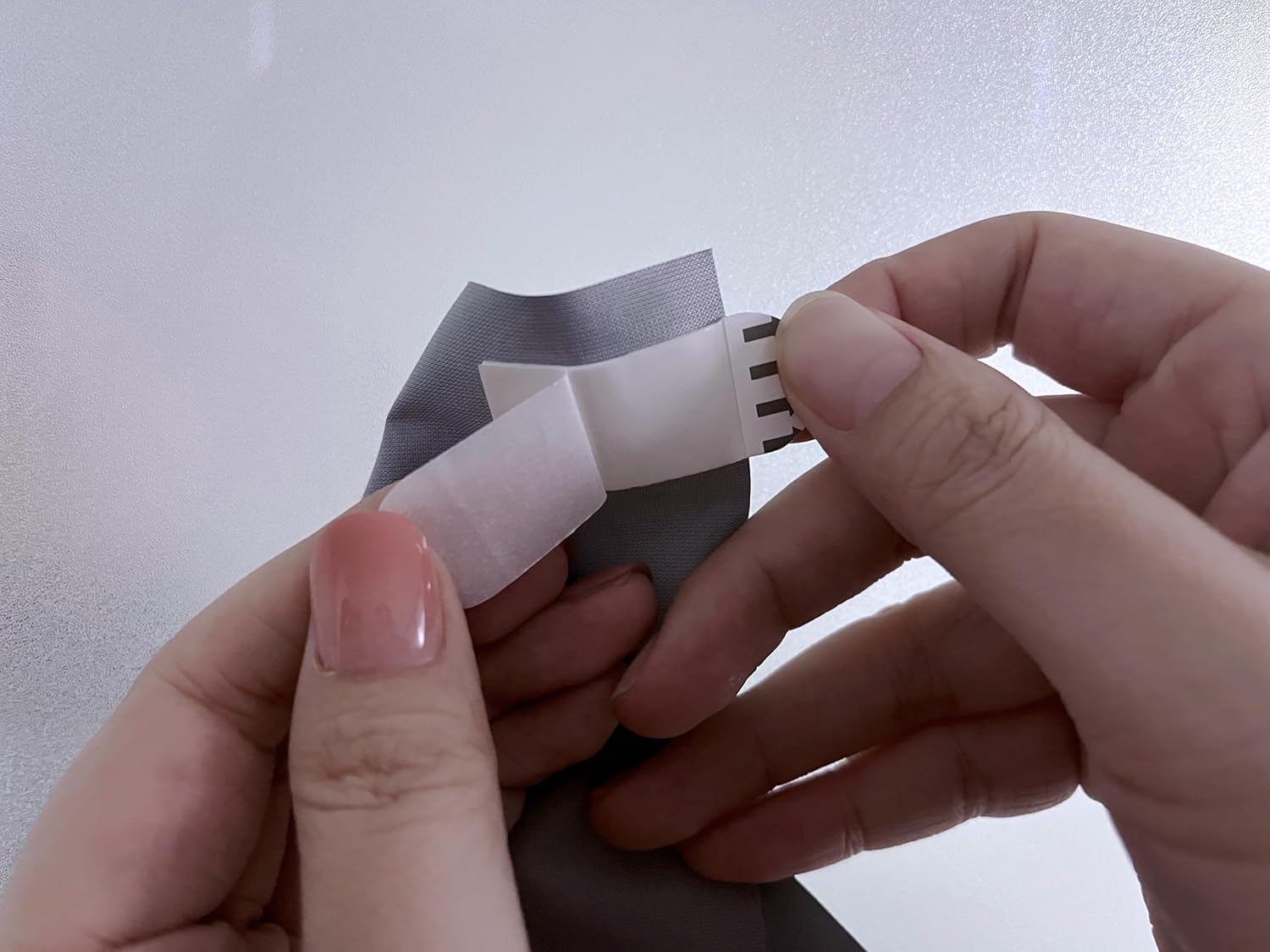 Hands peeling off the protective backing from a white adhesive strip attached to the projector screen.