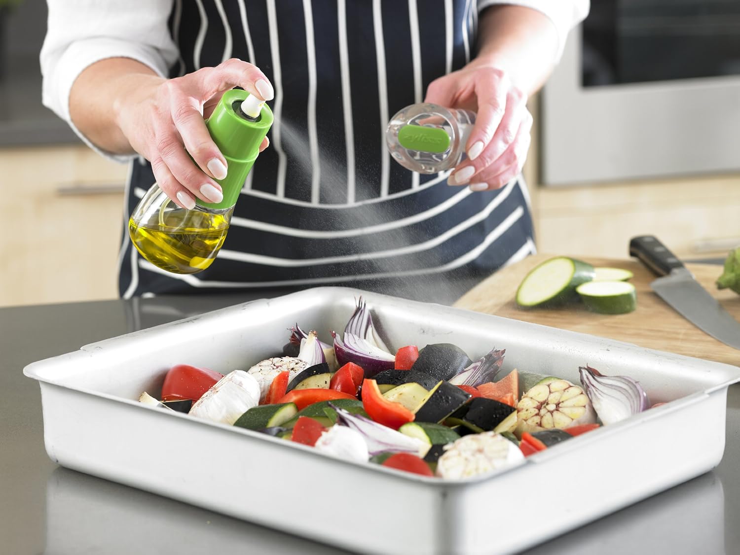 Person spraying oil onto vegetables in a baking tray