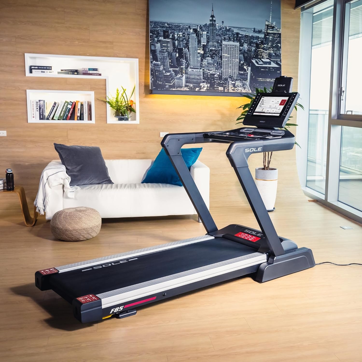 Sole F85 Folding Treadmill in Living Room Setting - Versatile Foldable Home Workout Equipment Sole Fitness F85 folding treadmill in a stylish modern living room with white sofa, bookshelves, plants, and city skyline wall art, showcasing compact home fitness integration