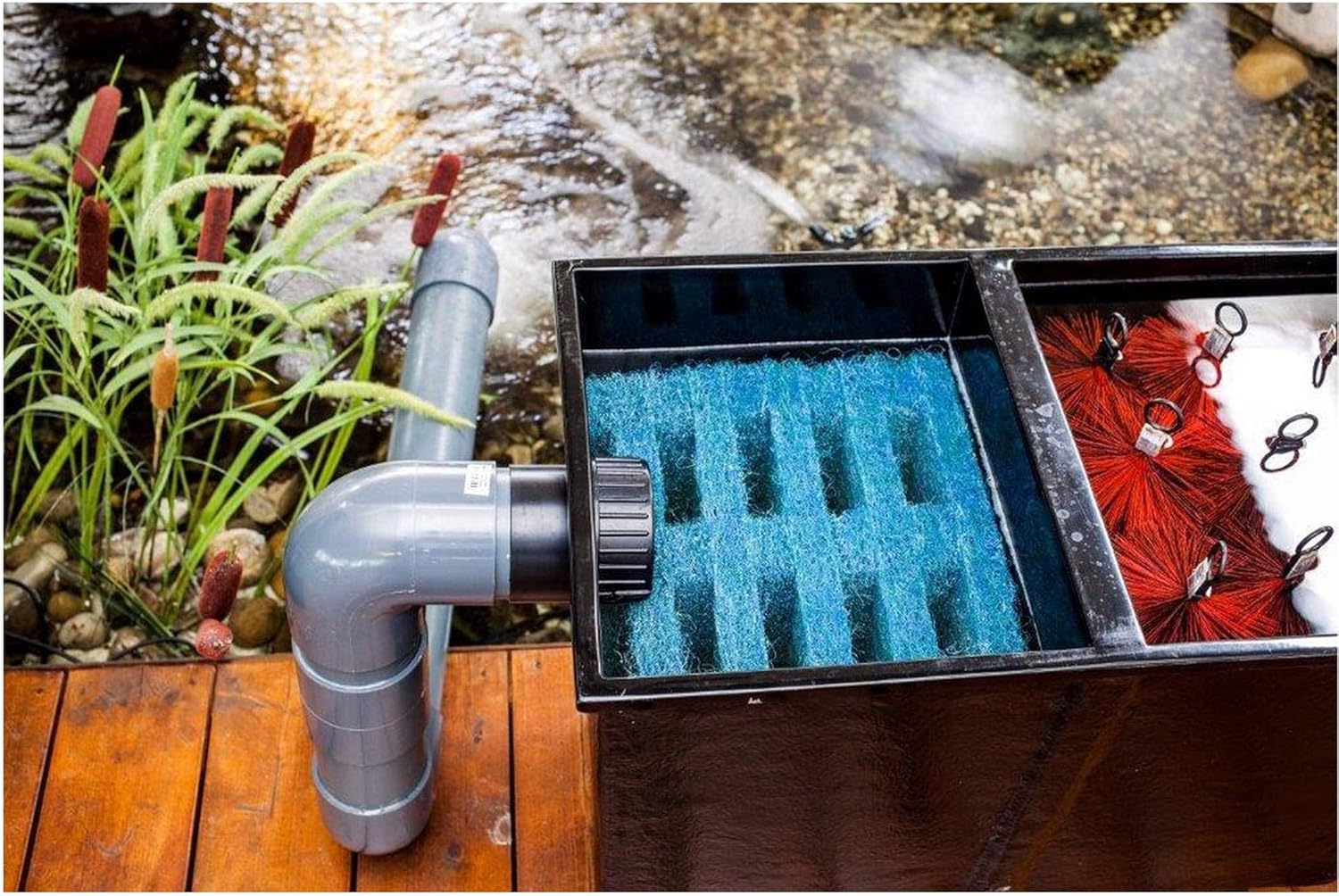 Top-down view of the Heissner Apollo XXL PRO pond filter installed next to a pond, with inlet and outlet pipes connected.