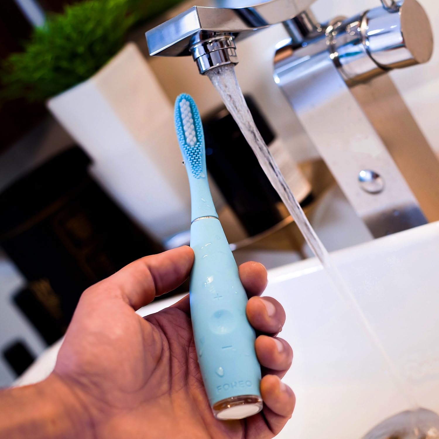 Hand holding FOREO ISSA 2 toothbrush under running water for cleaning