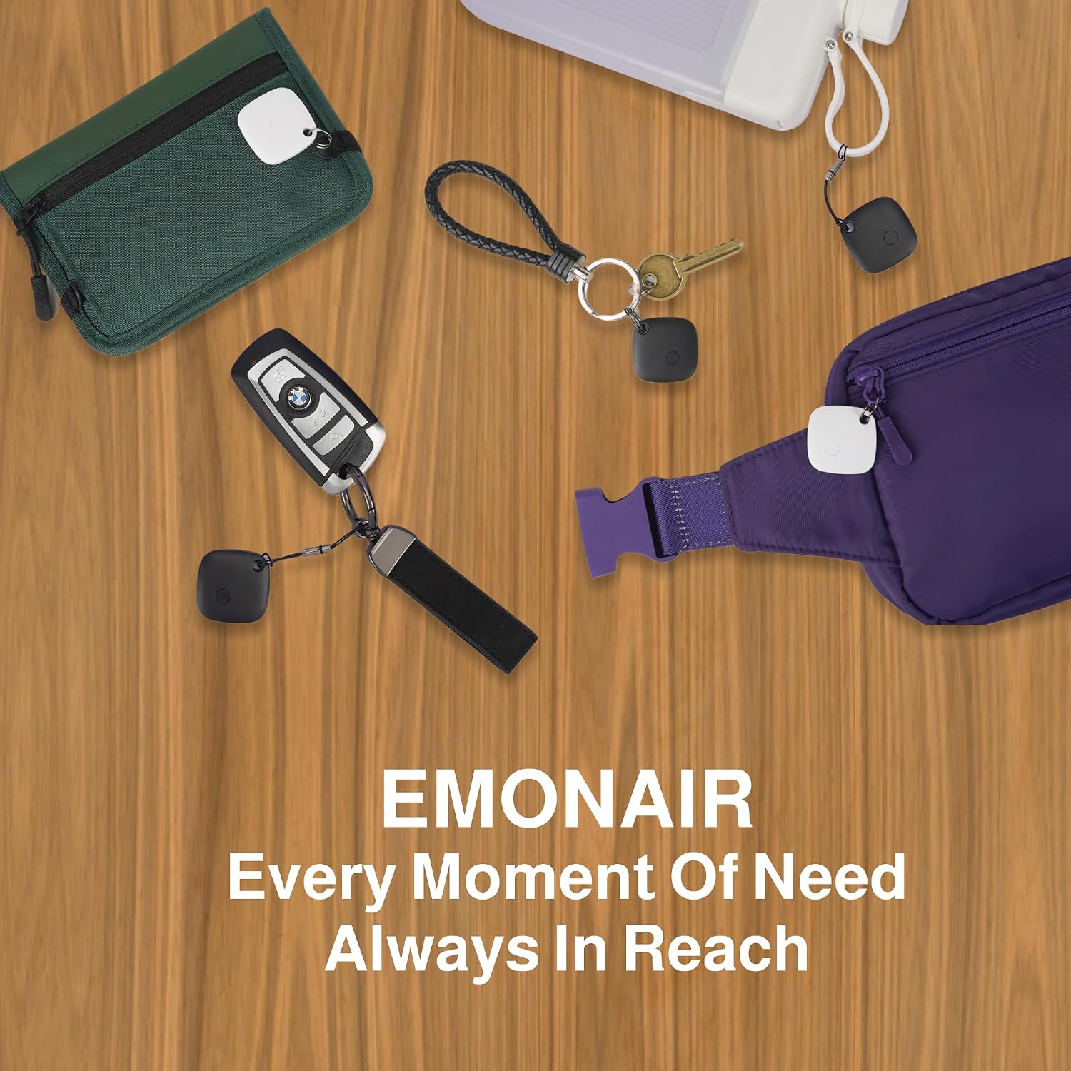 Several EMONAIR Mate Tracker Tags attached to various personal items like a wallet, keys, and a fanny pack, on a wooden surface.