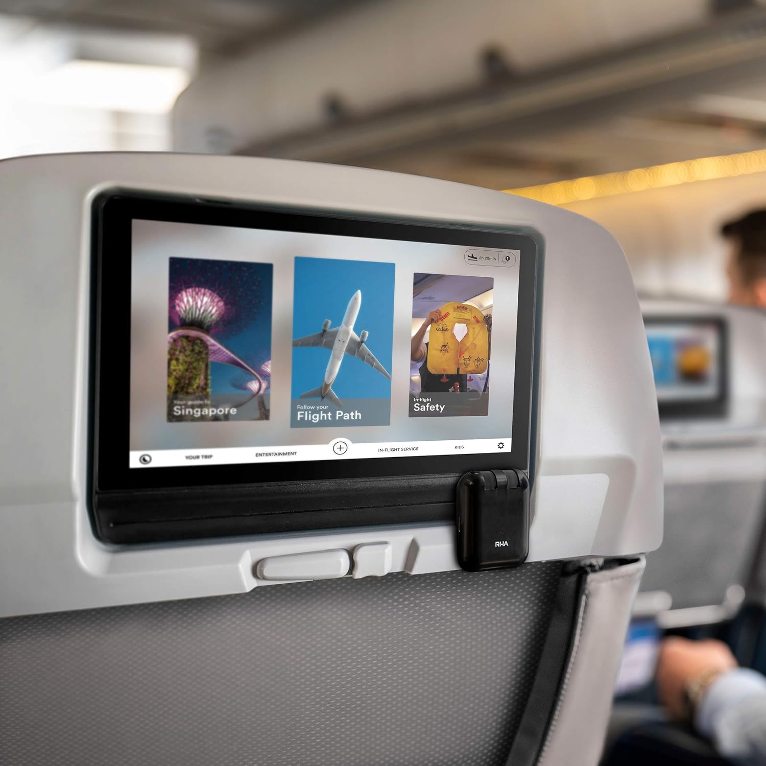 RHA Wireless Flight Adapter plugged into an in-flight entertainment screen, with a person wearing wireless headphones.