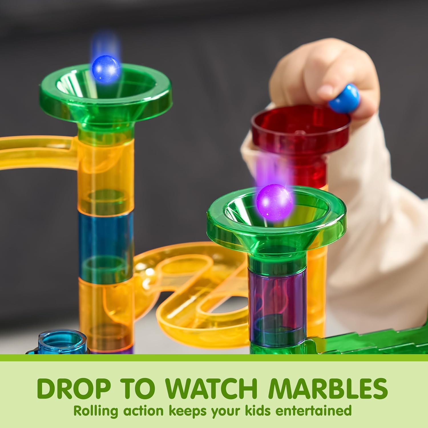 A child's hand dropping a glowing marble into the top funnel of a colorful marble run.
