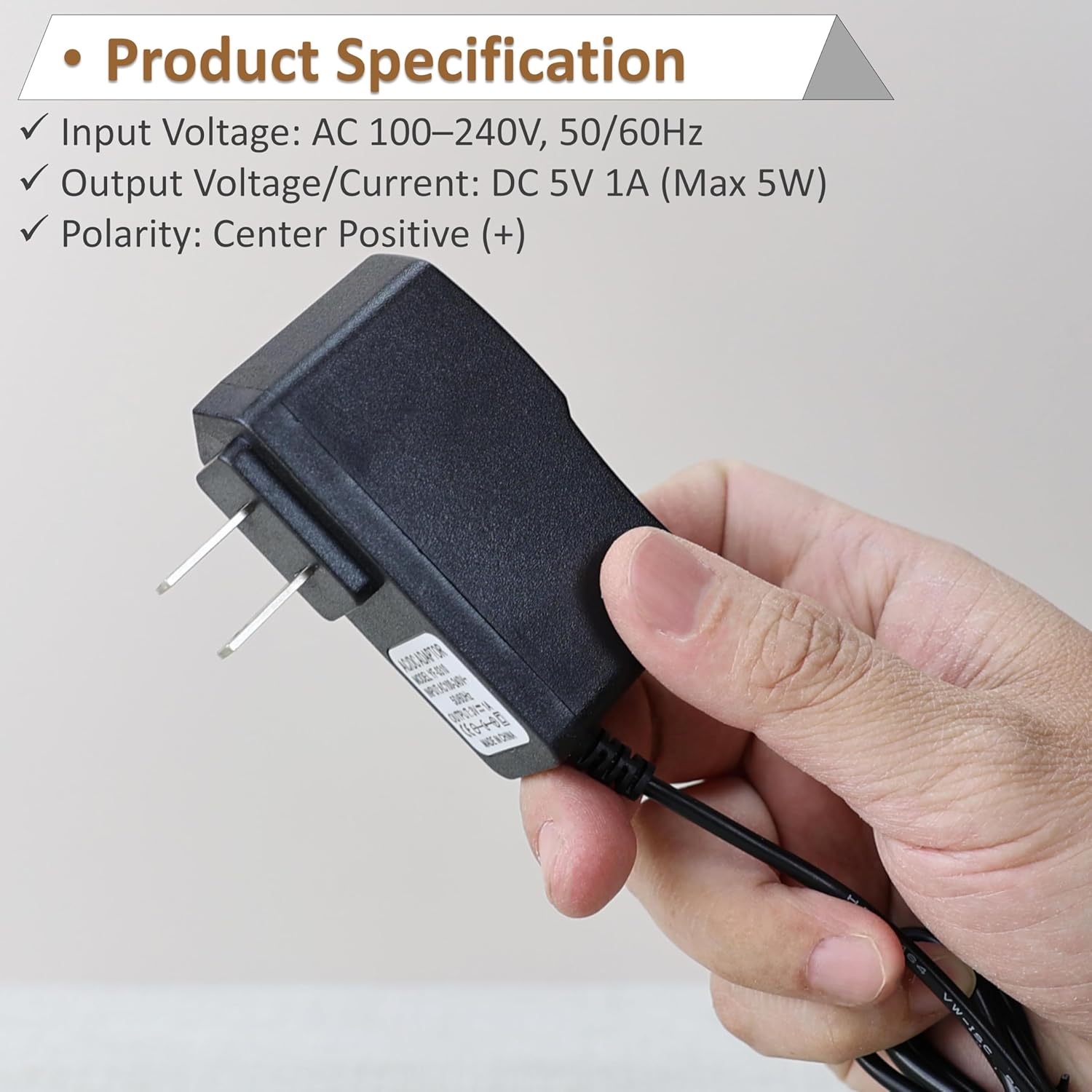 Image showing the power adapter held in a hand, with text overlay detailing input voltagе, оутпут волtage/current, and polarity.