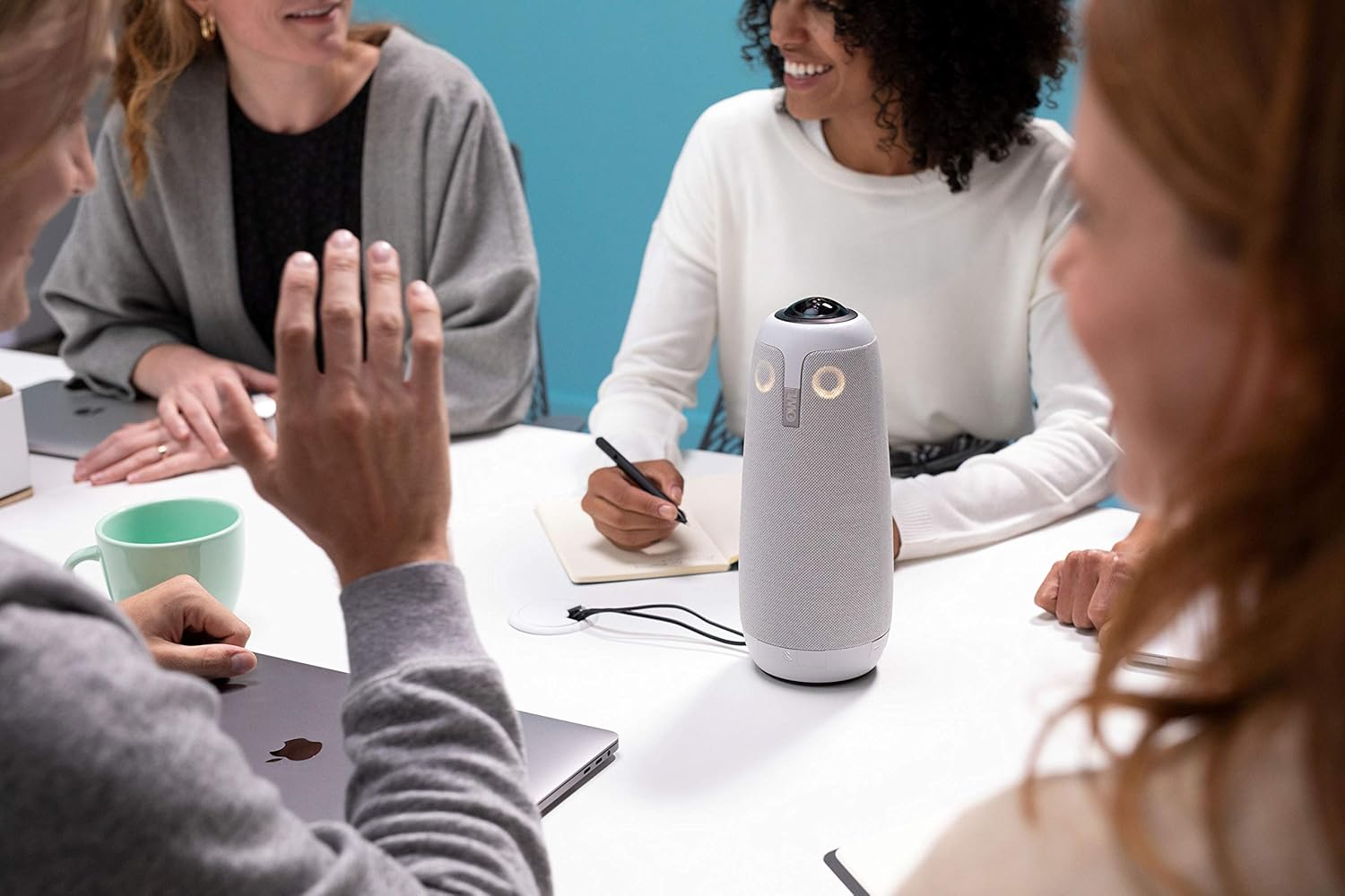 Close-up of the Meeting Owl Pro on a table with people interacting around it, demonstrating its central placement.
