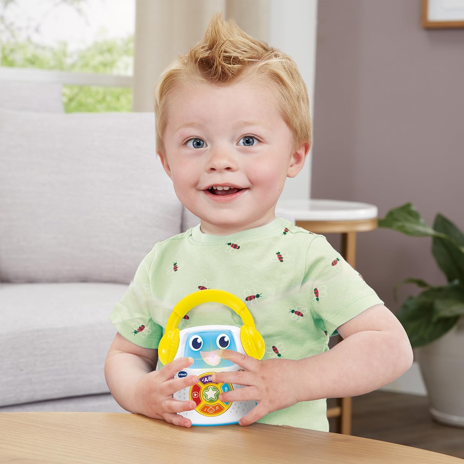 Toddler boy holding the VTech Baby's First Music Player on a table, smiling.