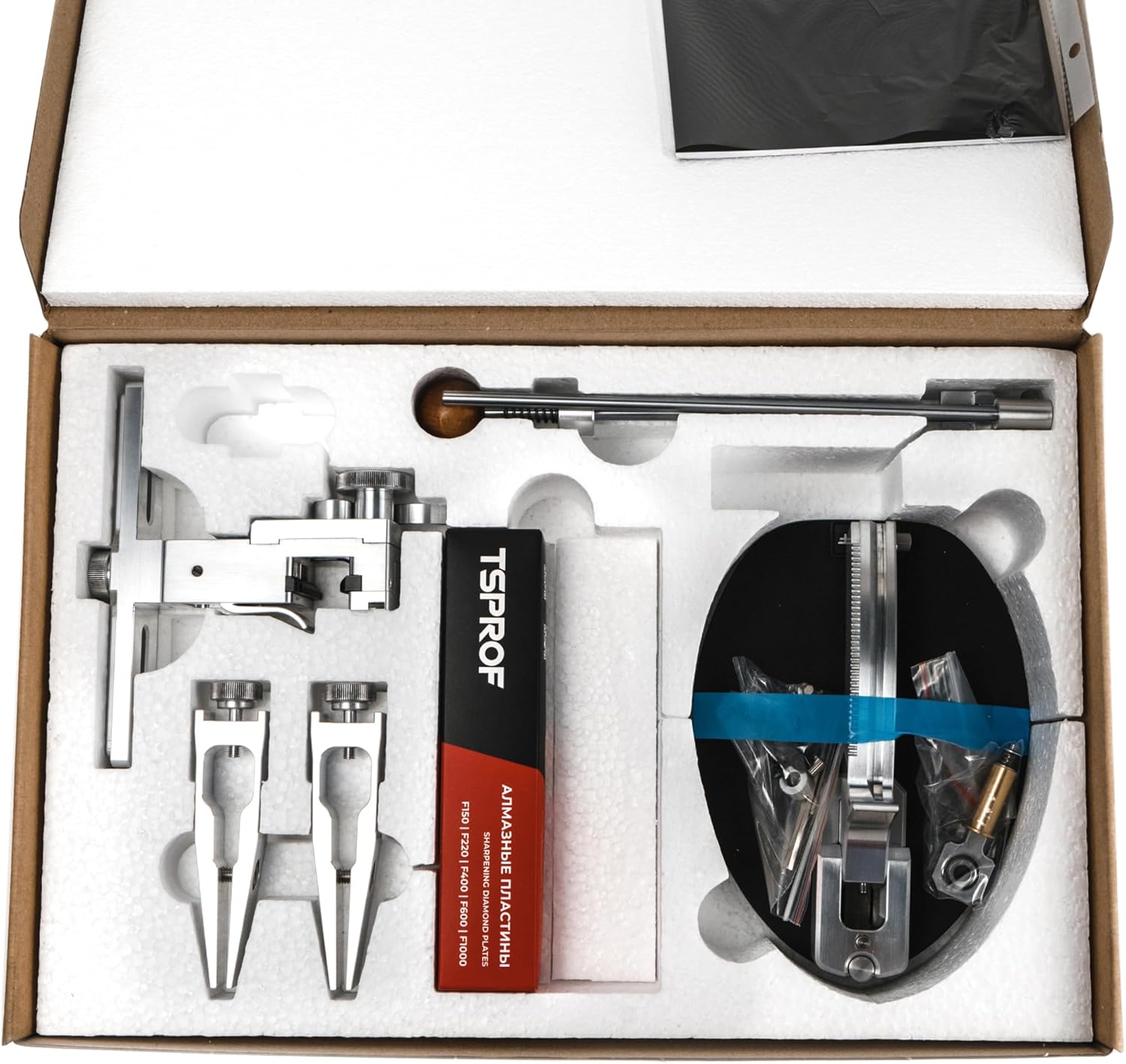 Contents of the TSPROF Kadet Pro Sharpening Kit in its box, showing the main unit, clamps, guide rod, and sharpening stones.