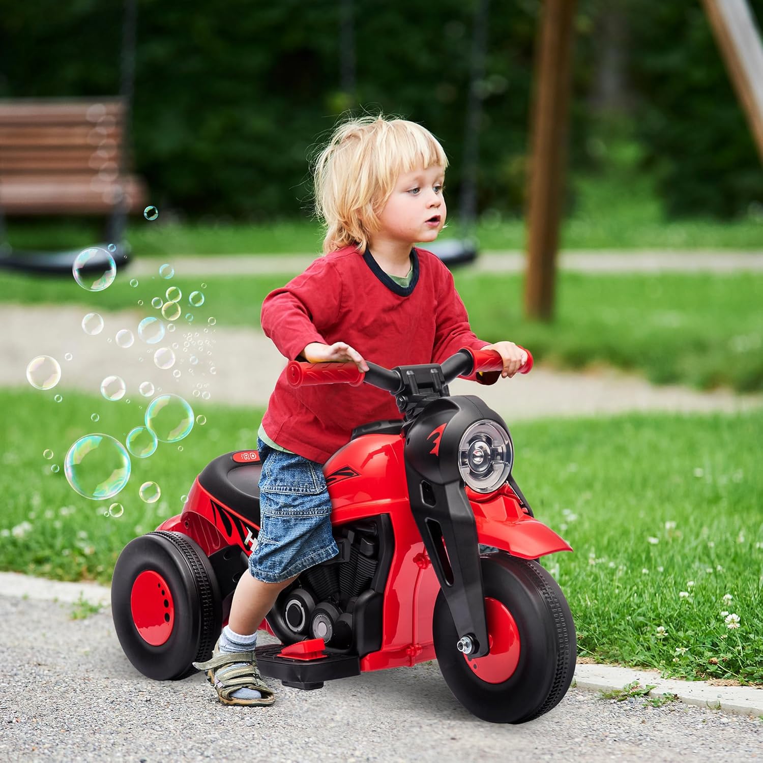A young child riding the red Qaba Ride on Bubble Car outdoors on a paved path, with bubbles floating around.