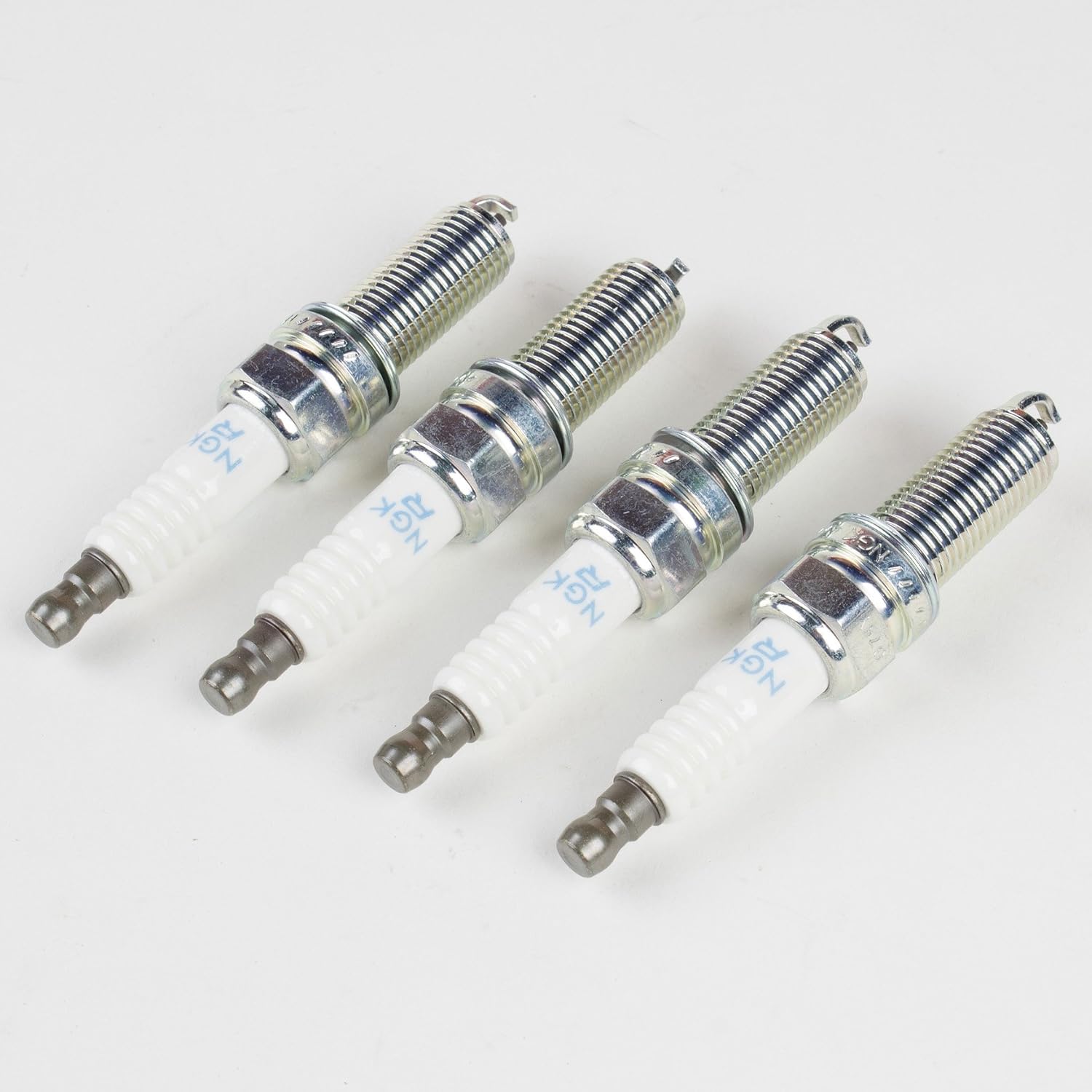 Four individual Genuine OEM Kia (Hyundai) NGK Spark Plugs laid out on a white surface.