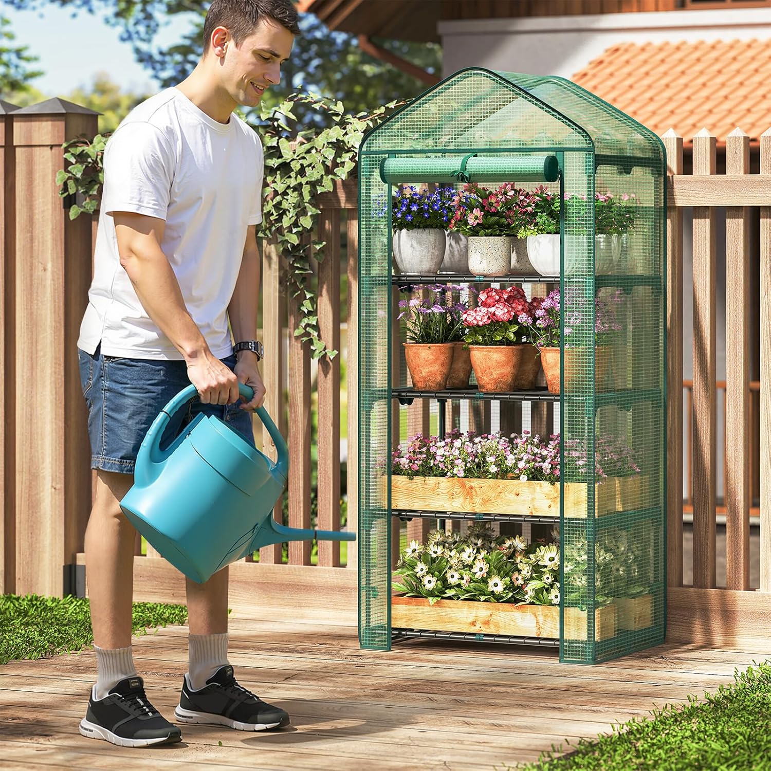 A person watering plants inside the greenhouse with a blue watering can.