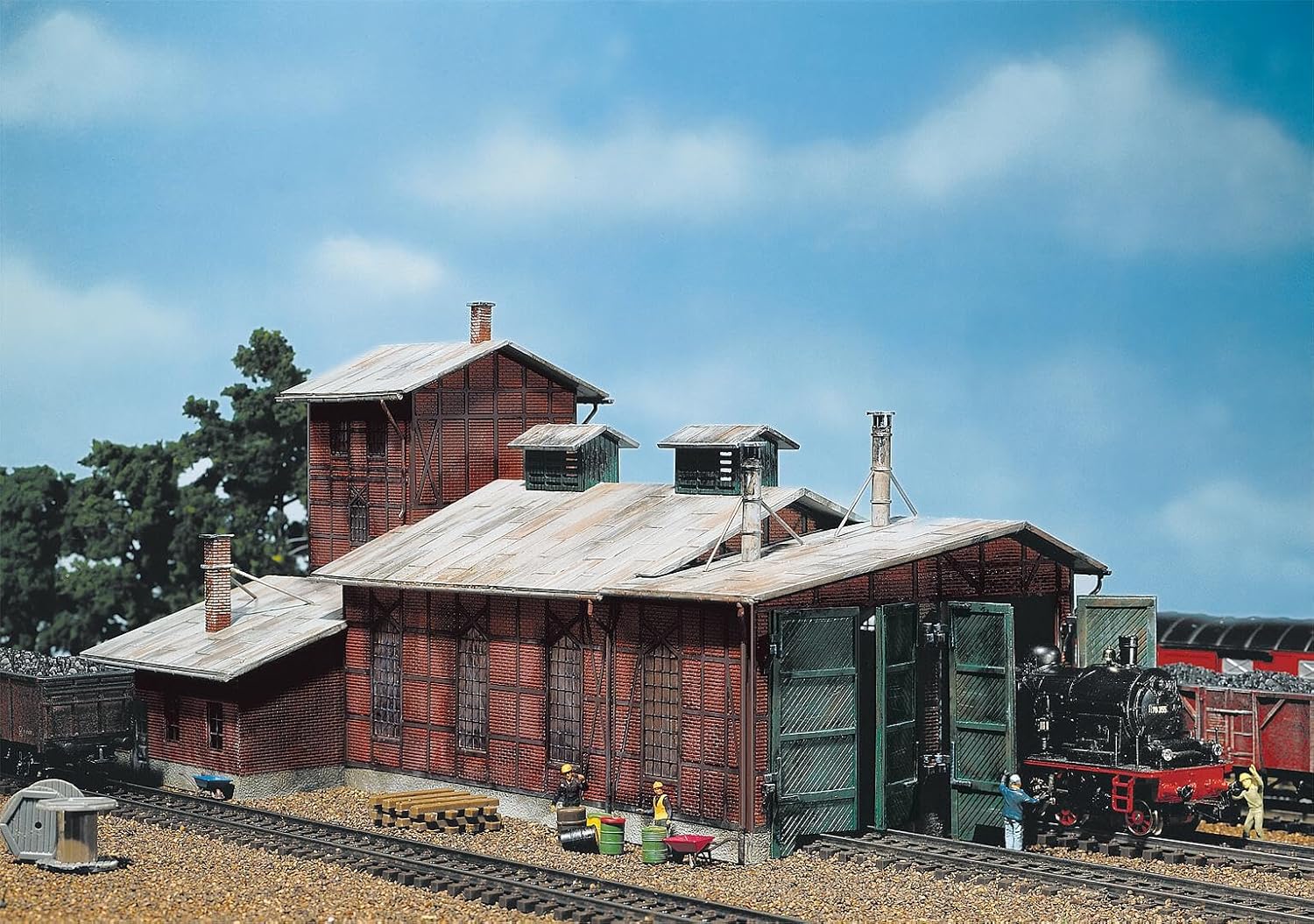വിശാലമായ view of the assembled Faller 120161 Enginehouse within a model railway diorama, showing surrounding tracks and scenery.