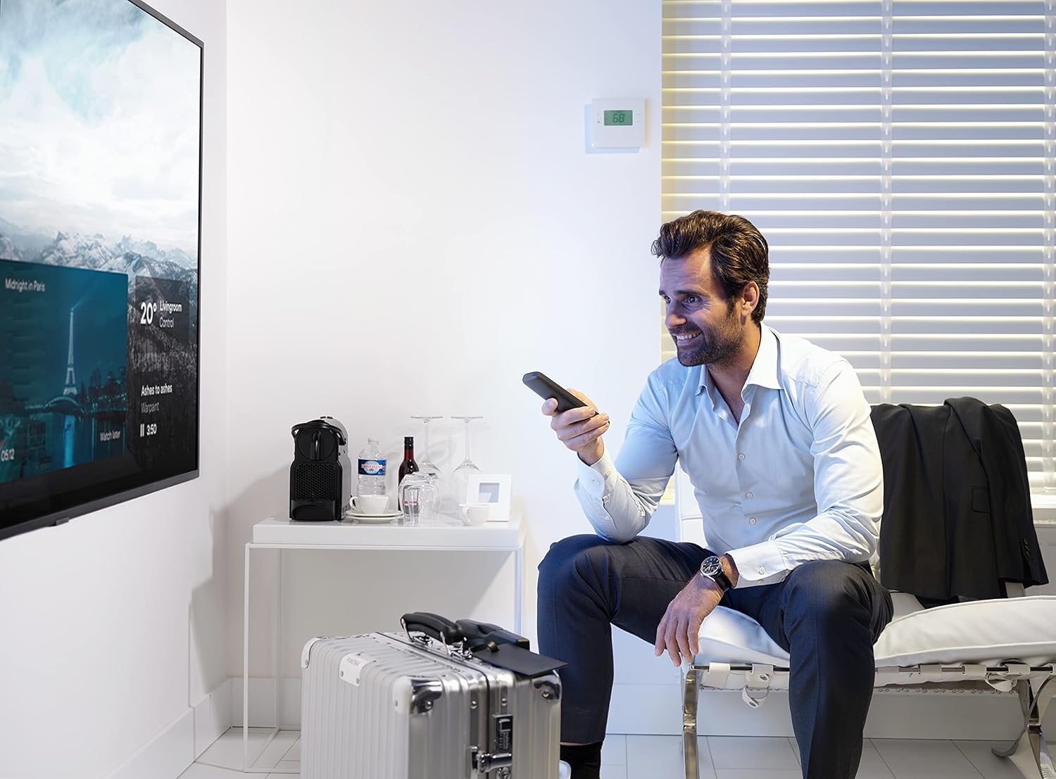 A man comfortably using the One For All Slate R18200 remote control in a hotel room setting.