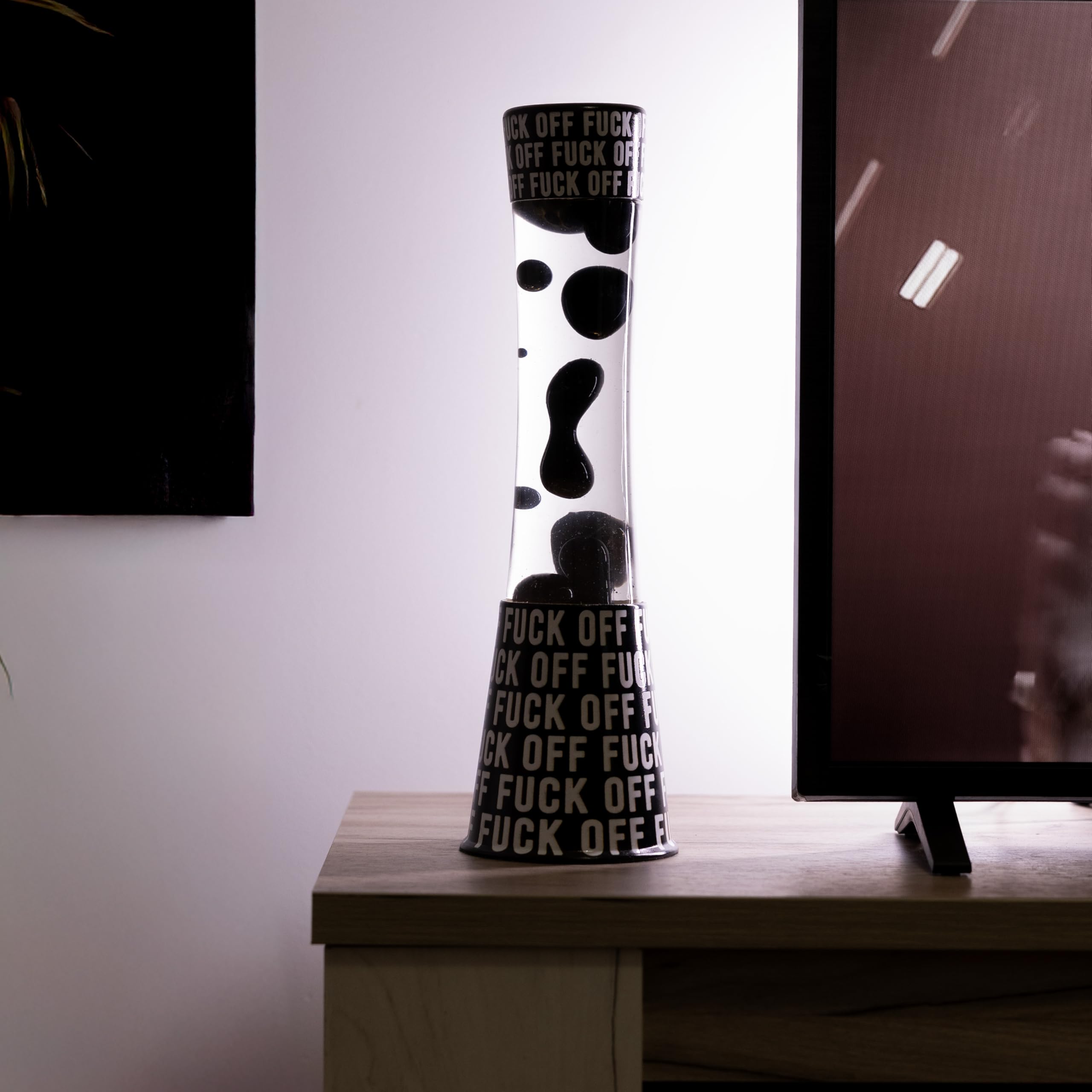 Fisura - Lampa lawa "f*ck off". Czarna podstawa z napisem, przezroczysty płyn i czarna lawa. Relaksujący efekt. Z zapasową żarówką. 11 cm x 11 cm x 39,5 cm.