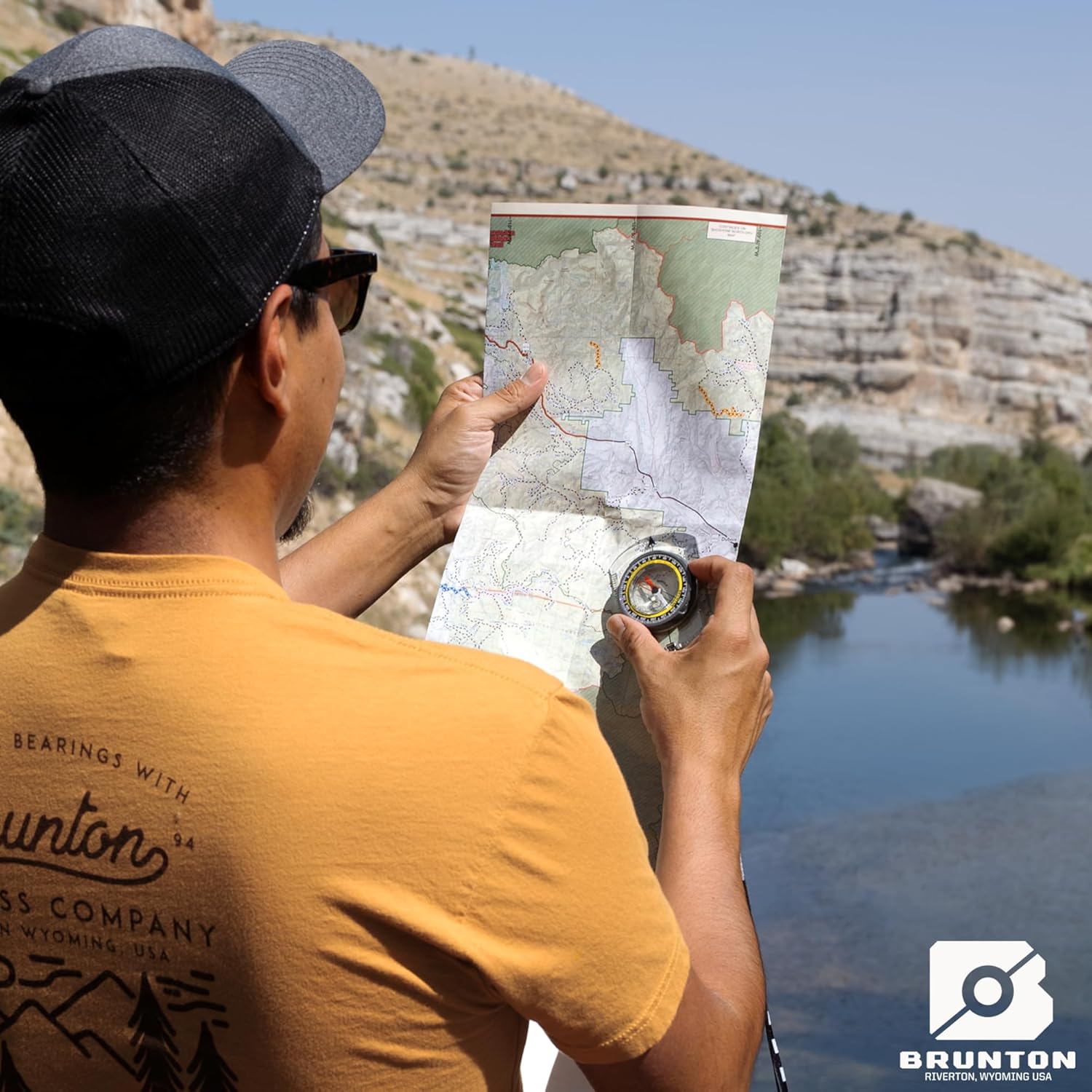 A person holding a Brunton TruArc 3 compass and a map, aligning them for navigation in an outdoor setting.