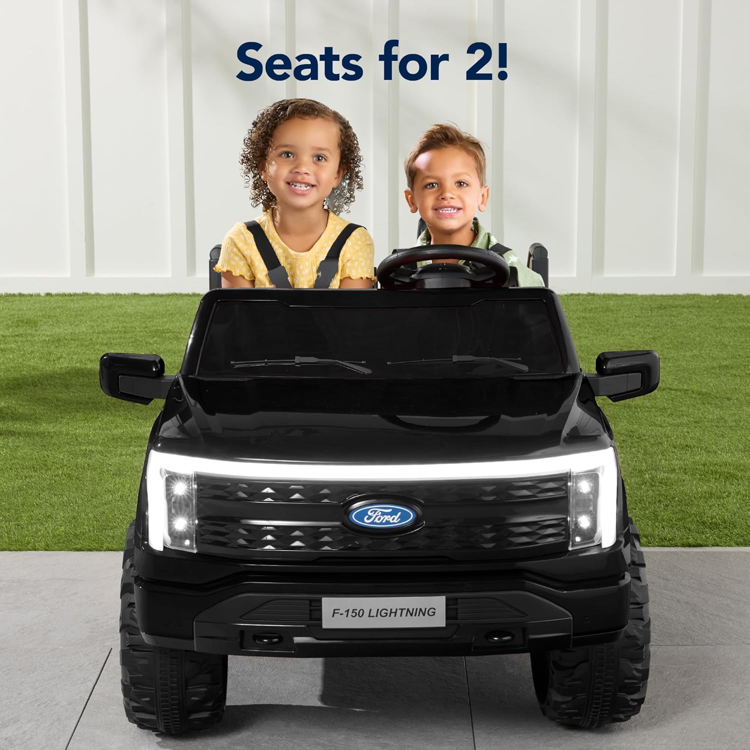 Two children seated in the black Ford F-150 Lightning ride-on truck, demonstrating its two-seater capacity.