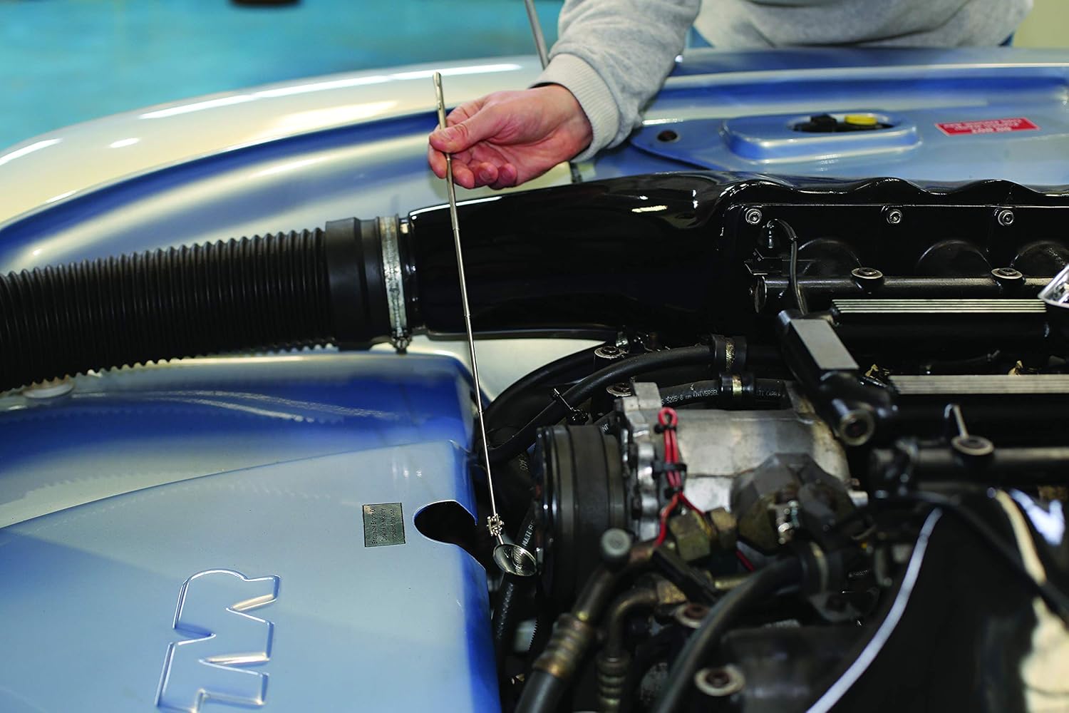 Hand using the inspection mirror to view a hidden area within an engine compartment.