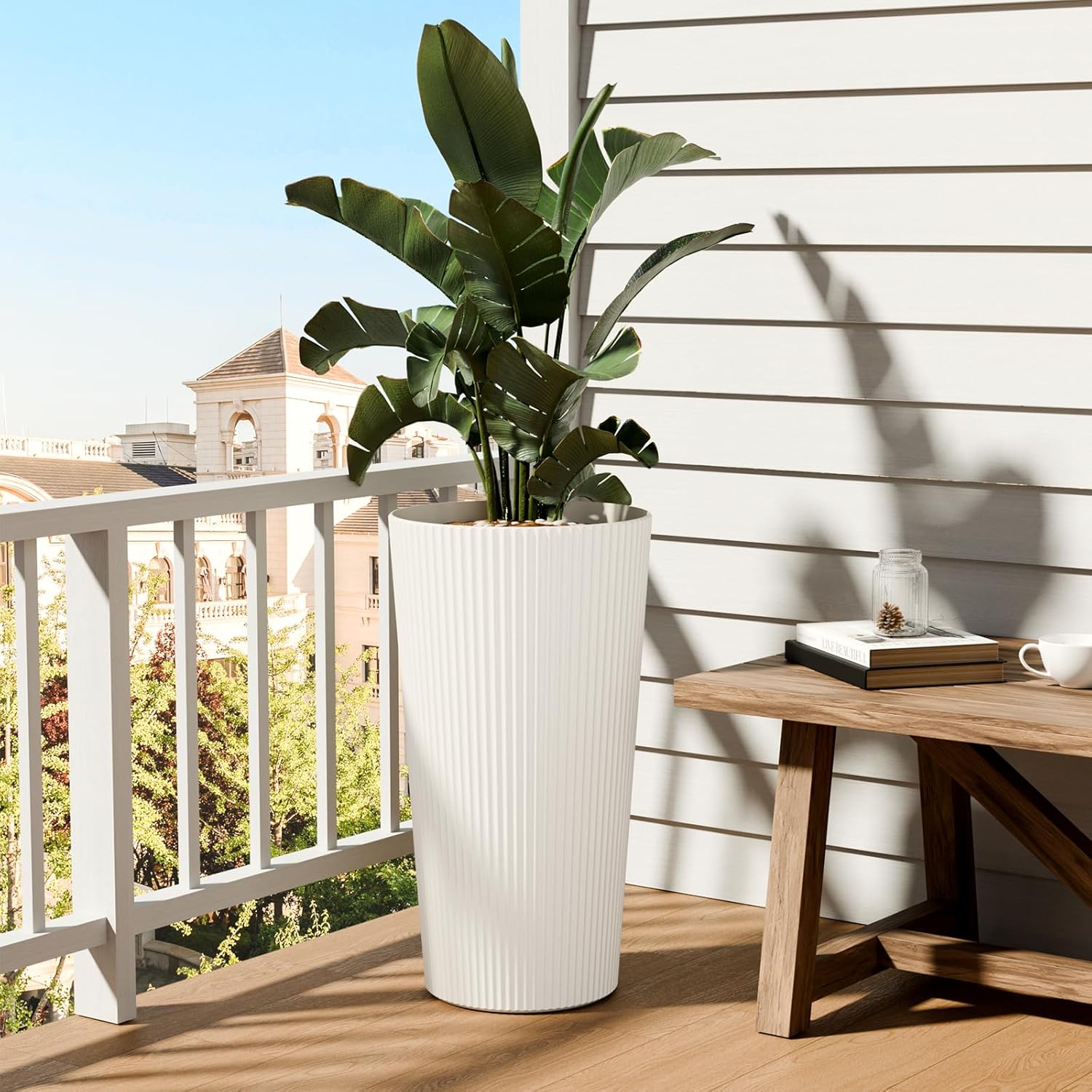 A FONTOI white striped planter with a large green plant placed on a sunny outdoor balcony.