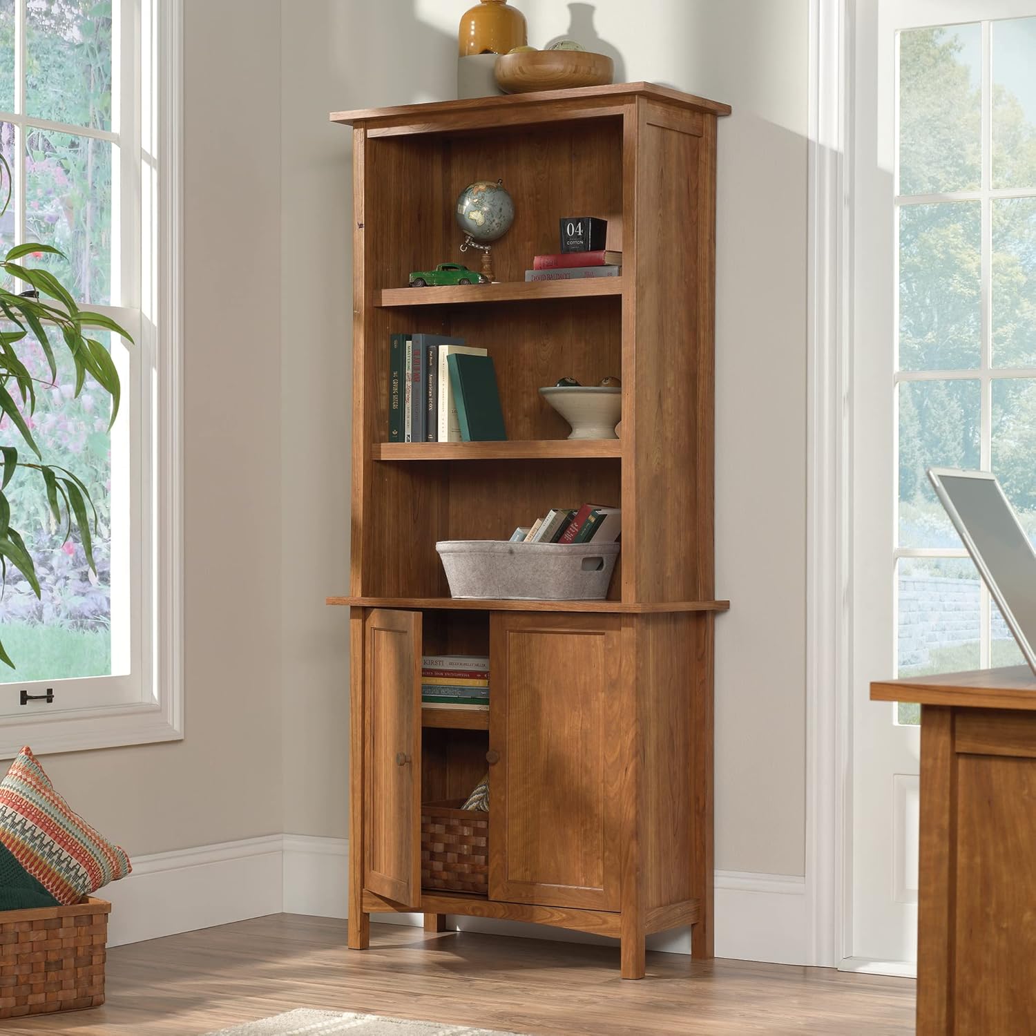 Sauder Union Plain Bookcase with one lower door open, revealing an adjustable shelf and stored items like books and a woven basket.